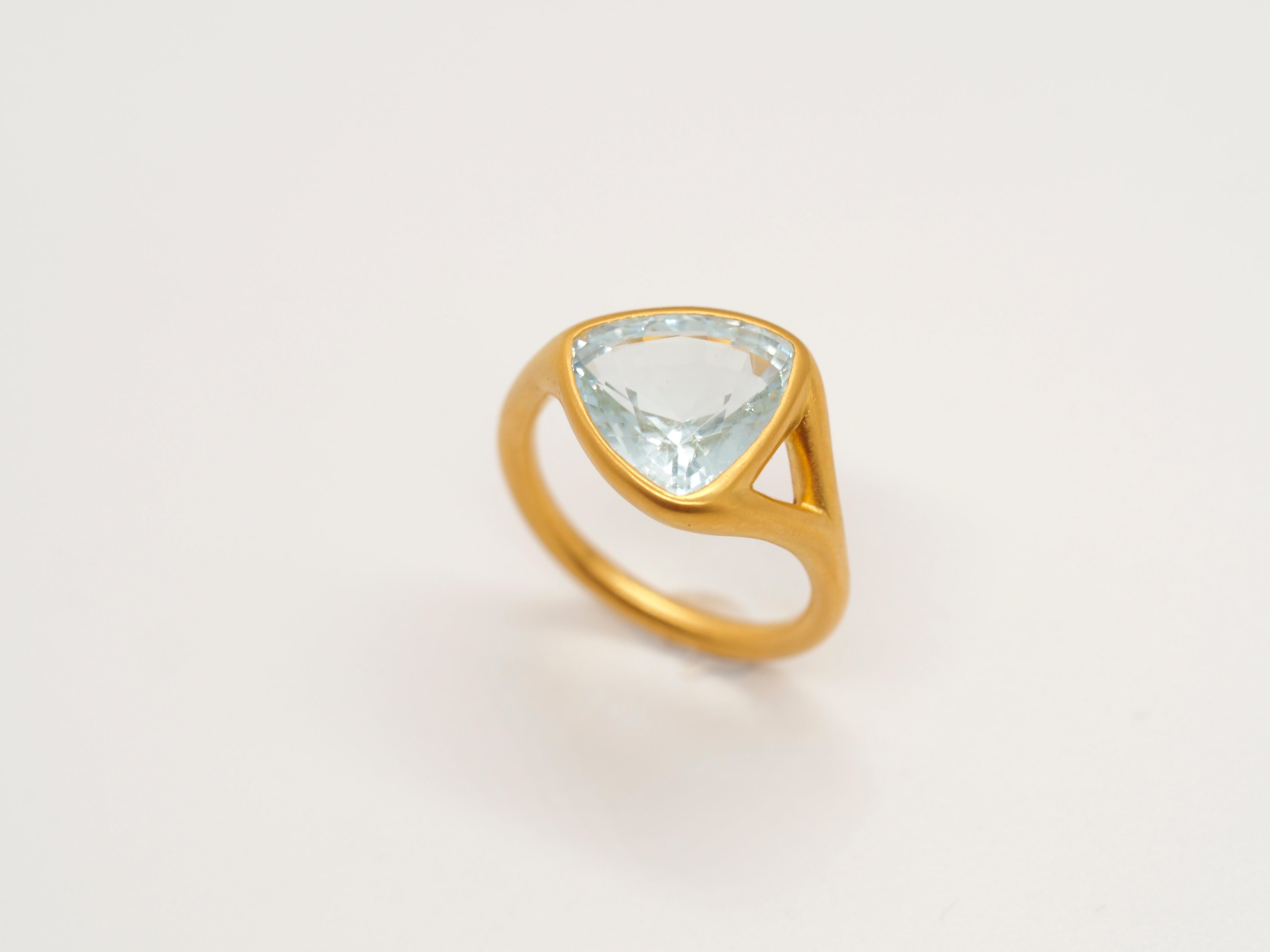 This modern & elegant ring by Scrives highlights a trillion shape aquamarine set in 22kt gold. The aquamarine of 4.6cts touches directly the finger. 
The aquamarine comes from Myanmar. It is a natural stone from the beryl family. It has a light blue