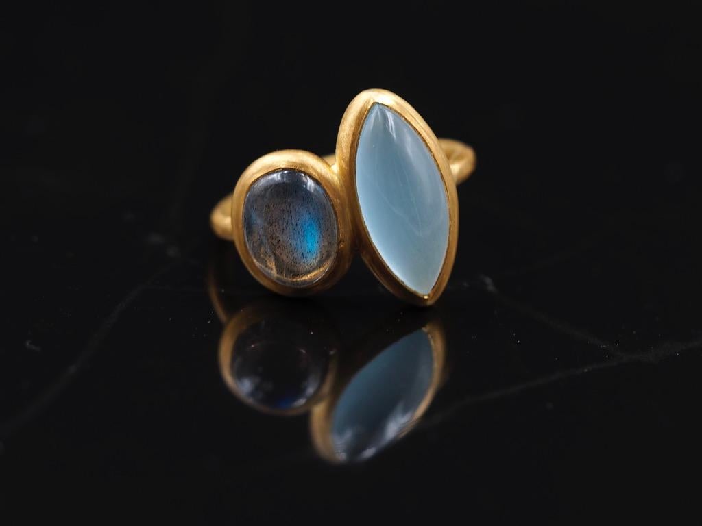 Dieser Ring von Scrives besteht aus einem ovalen Labradorit-Cabochon und einem großen marquiseförmigen Aquamarin-Cabochon. Der Labradorit hat einen stark blauen Farbton. 
Die Steine sind in einer geschlossenen 22-karätigen Goldfassung gefasst.
Sie