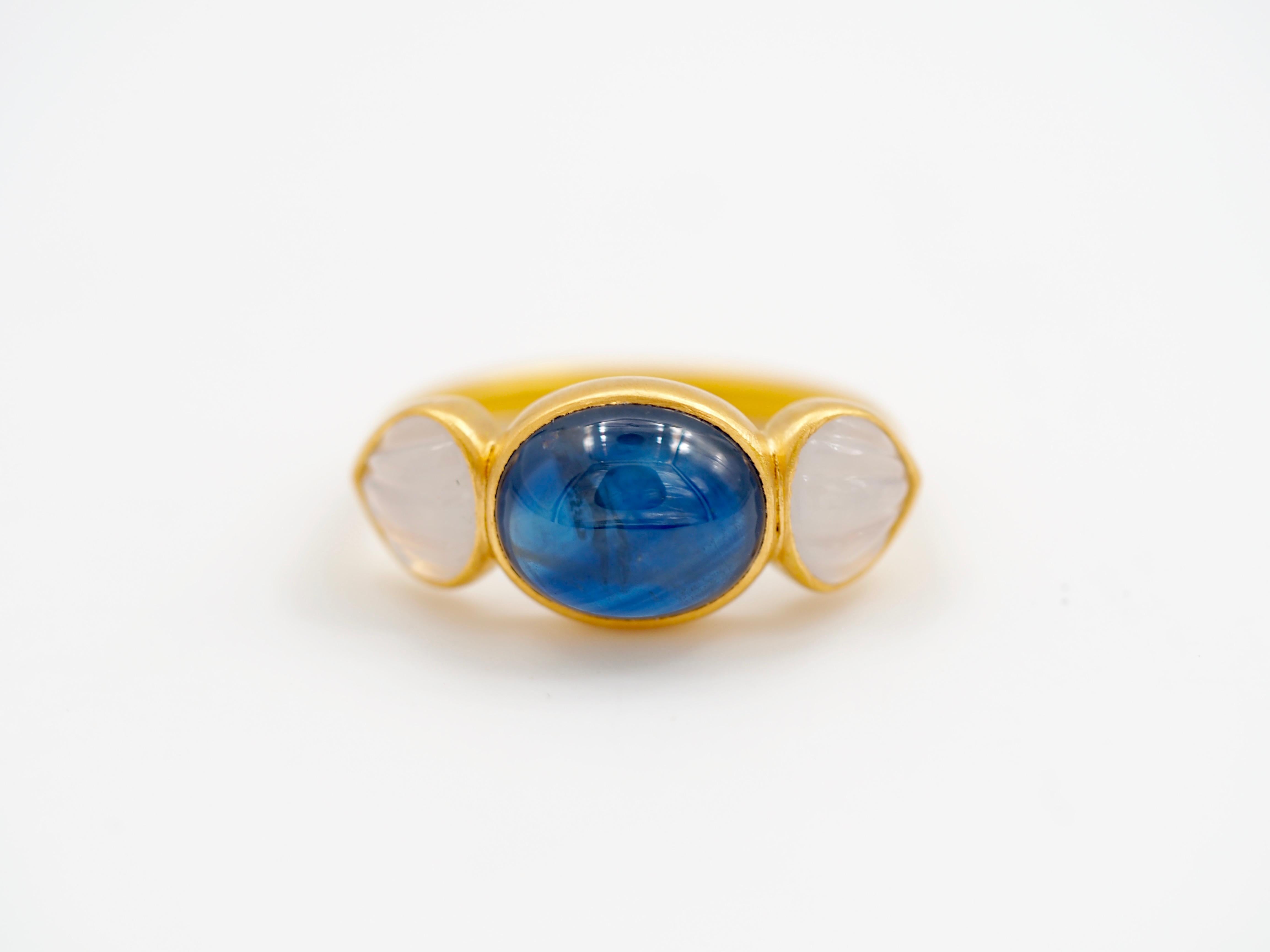 Dieser zarte Ring besteht aus einem tiefblauen natürlichen Saphir-Cabochon von 7,58 ct, umgeben von 2 weißen Chalcedonen, die wie Muscheln geschnitzt sind (insgesamt 1,87 ct). Der Saphir ist naturbelassen mit typischen Einschlüssen und zeigt