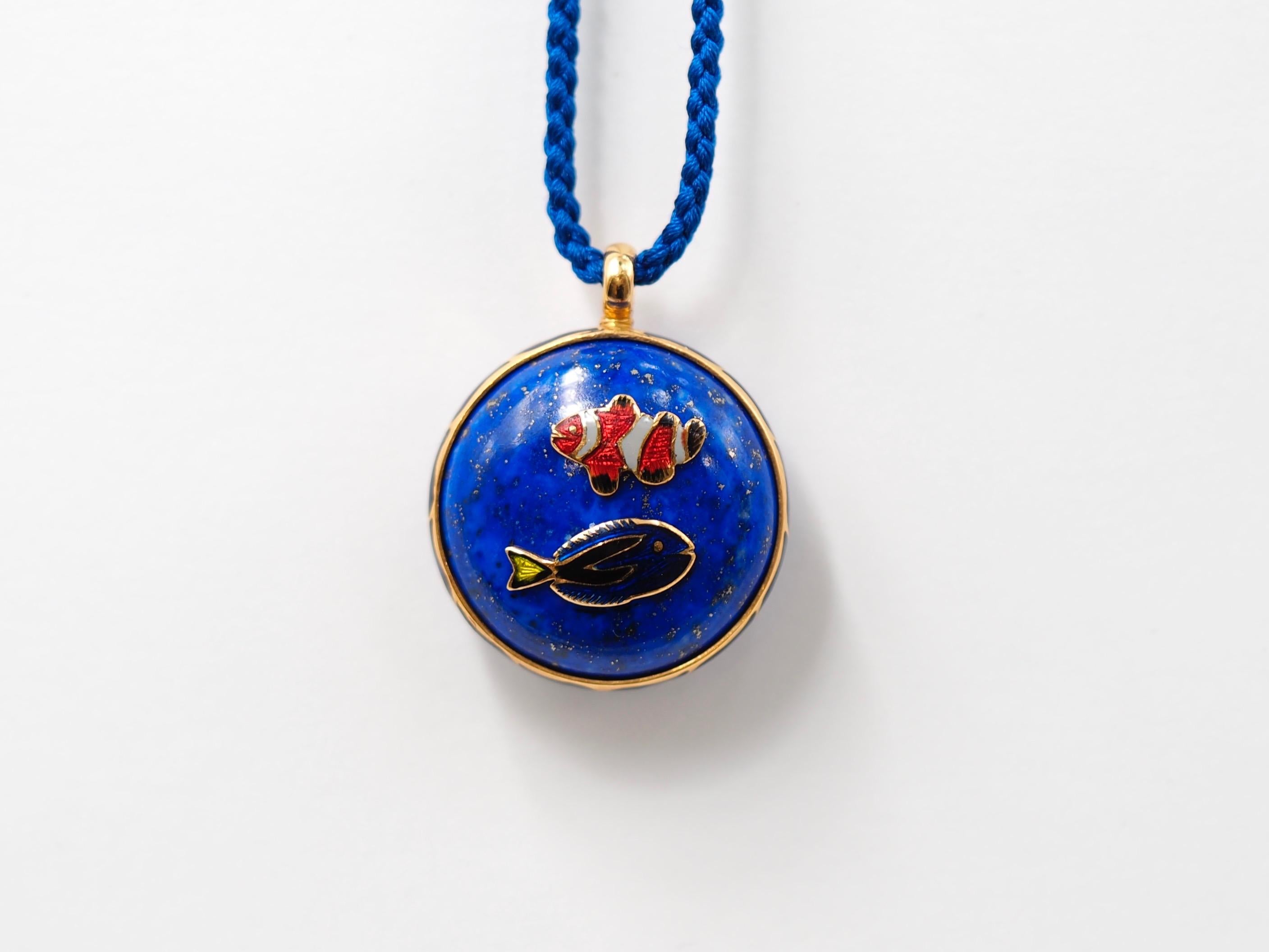 This one-of-a-kind pendant by Scrives is composed of a lapis lazuli disk set in a 23kt gold round band with blue waves of hot and transparent enamel (Mina Kari). On one side of the lapis, 2 fishes in gold and mina kari are represented and on the