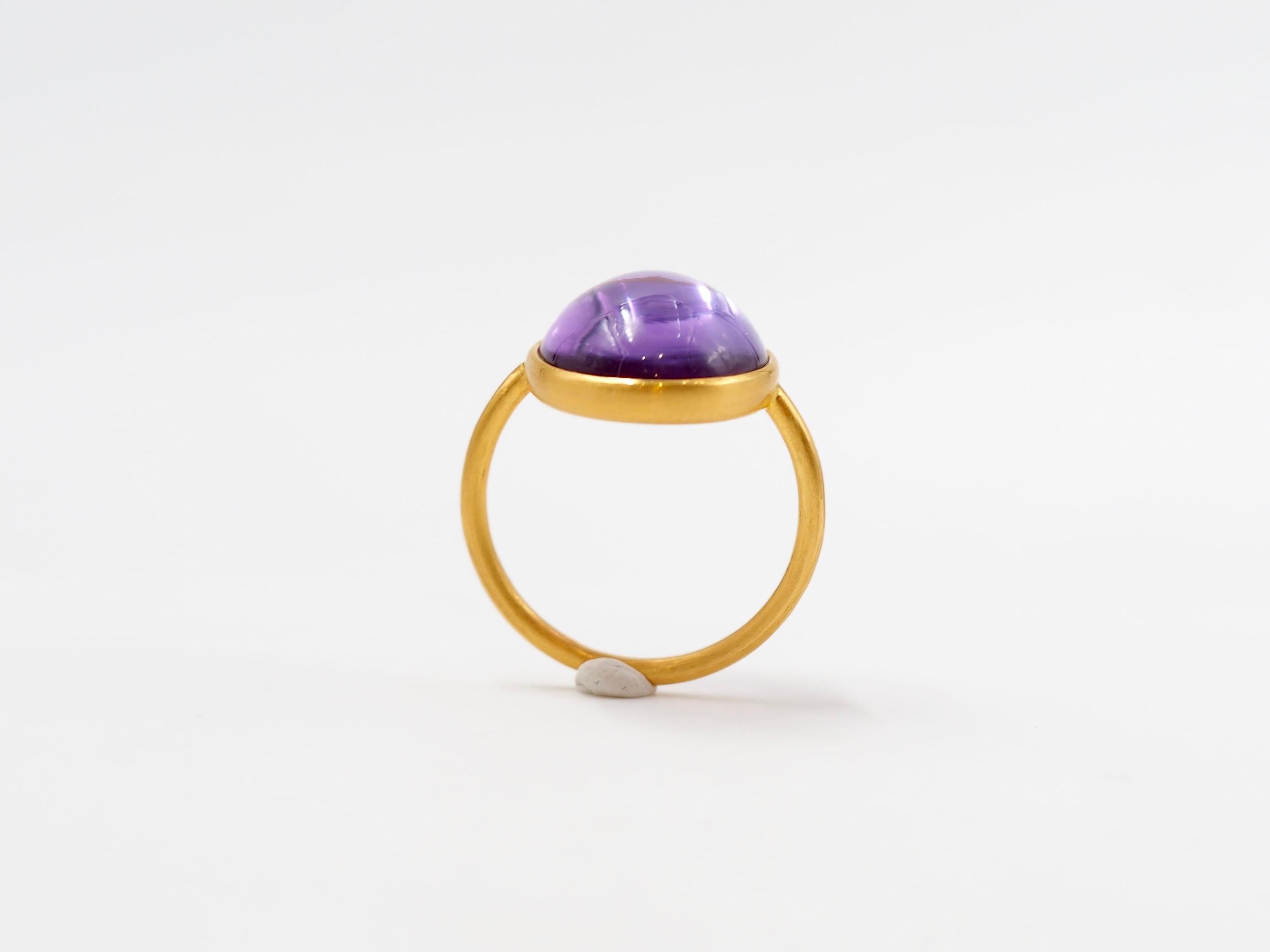 This simple ring by Scrives is composed of a large light colour cabochon amethyst of 11 cts. 
The stone is set in a 22kt closed gold setting.
This amethyst is natural and has not been treated. You can see that thanks to the slightly darker lines in