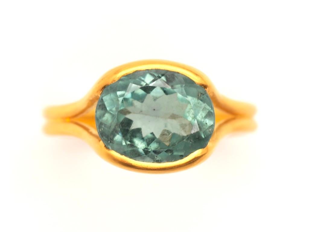 This delicate ring by Scrives is composed of a light blueish green (celadon colour) tourmaline of 3.69cts. The stone is hold by 2 gold lines that form the band. This design allows light to come into the stone from multiple directions and put into