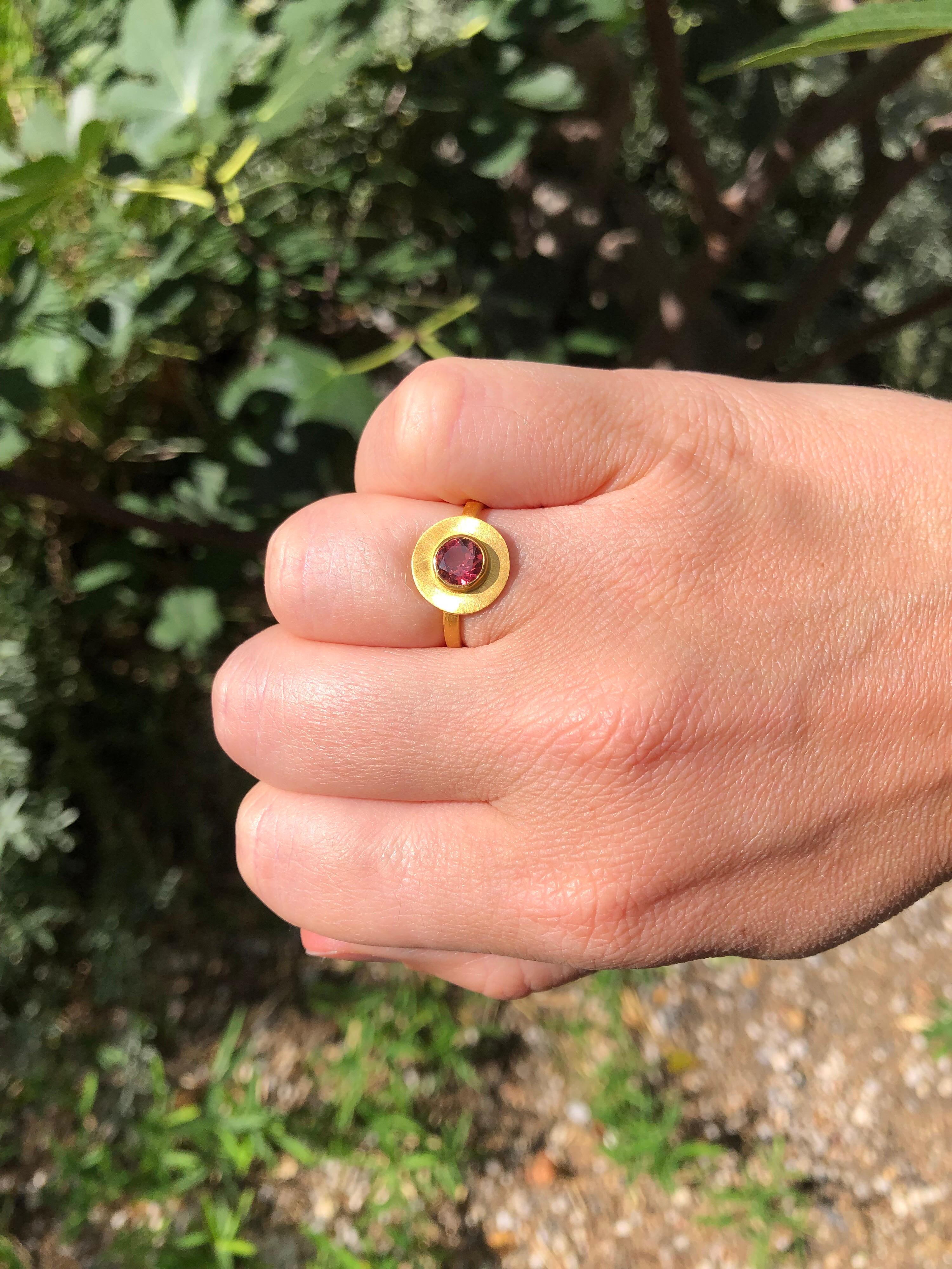 Scrives Sun Scheibenring besteht aus einem runden rosa Turmalin, der von einer großen Goldscheibe aus 22-karätigem Gold umgeben ist, die wie eine Sonne gebürstet ist. 
Diesen Ring gibt es auch mit einem Aquamarin.

Der Stein ist ein natürlicher,