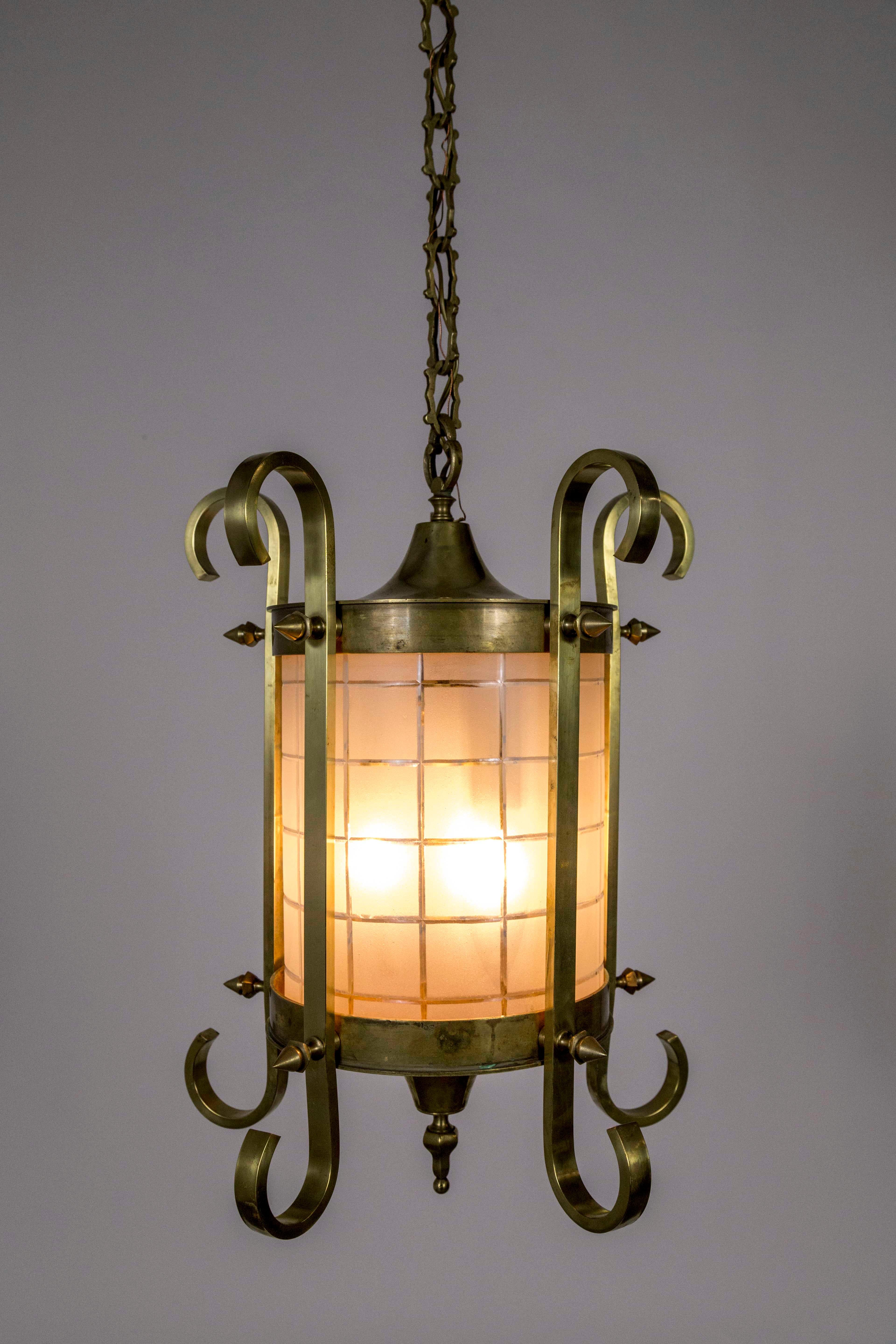 Brass and bronze lantern with unique, spike and scroll details from the 1920s, holding a beautifully hand etched, and beveled cylinder, glass shade. The decorative chain and ceiling canopy are original, American. Measures: 25” height x 17” diameter,