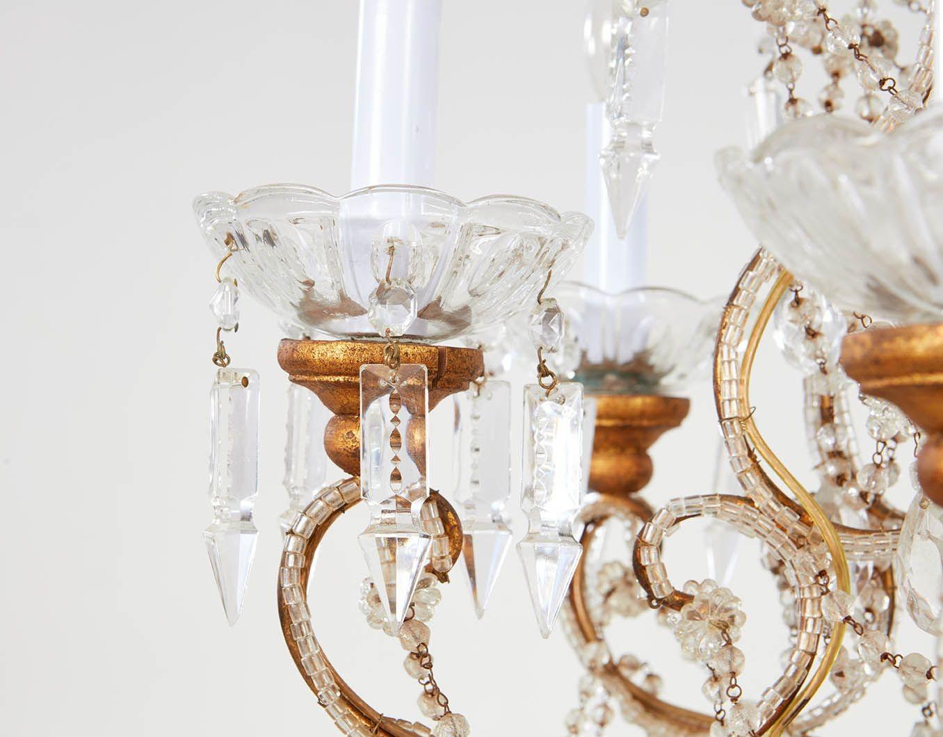 An opulent Italian chandelier having a scrolled gilt iron body adorned with glass beading and hanging crystals and teardrops, surmounted by a hollow striated glass finial and ending in a hanging solid faceted glass ball drop, with candle sockets in
