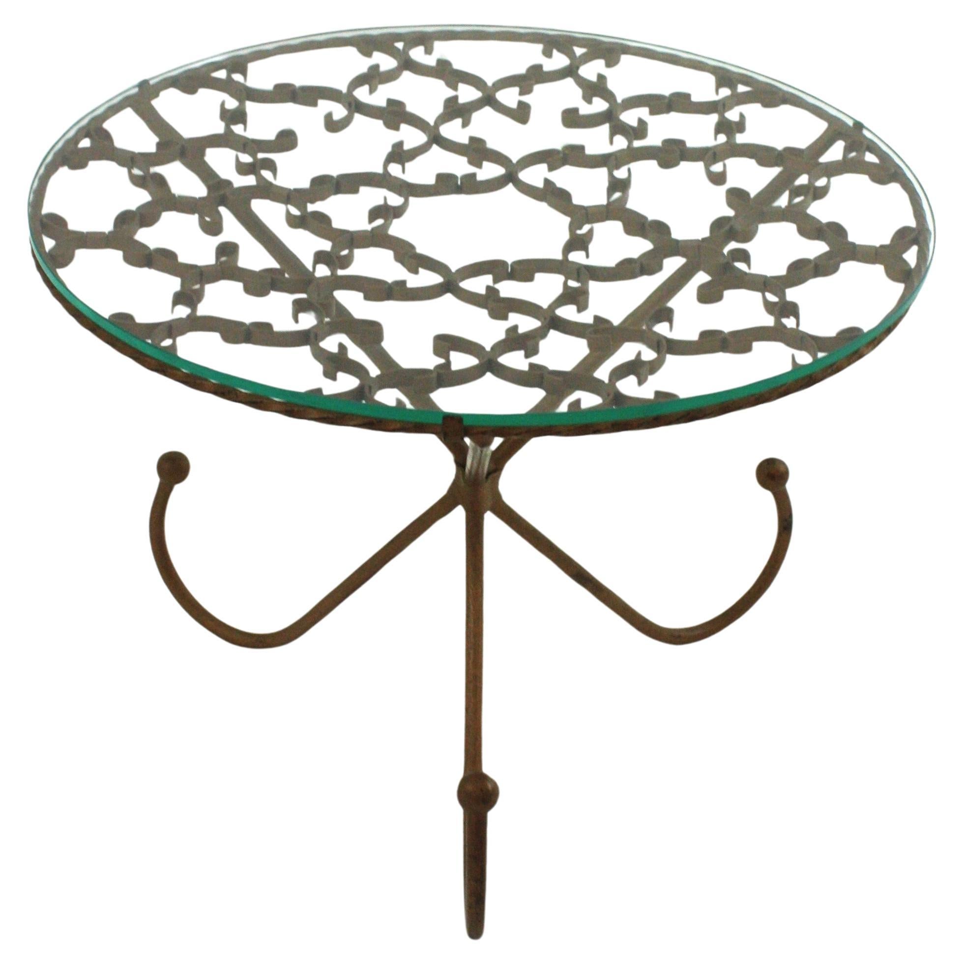 Spanish Round Coffee or Cocktails Table / Side Table with Scrollwork Design, 
Spain, 1950s
Materials: Iron, Glass
Eye-catching Hollywood Regency wrought gilt iron  tripod table with top adorned with scroll work details and glass top.
This beautiful