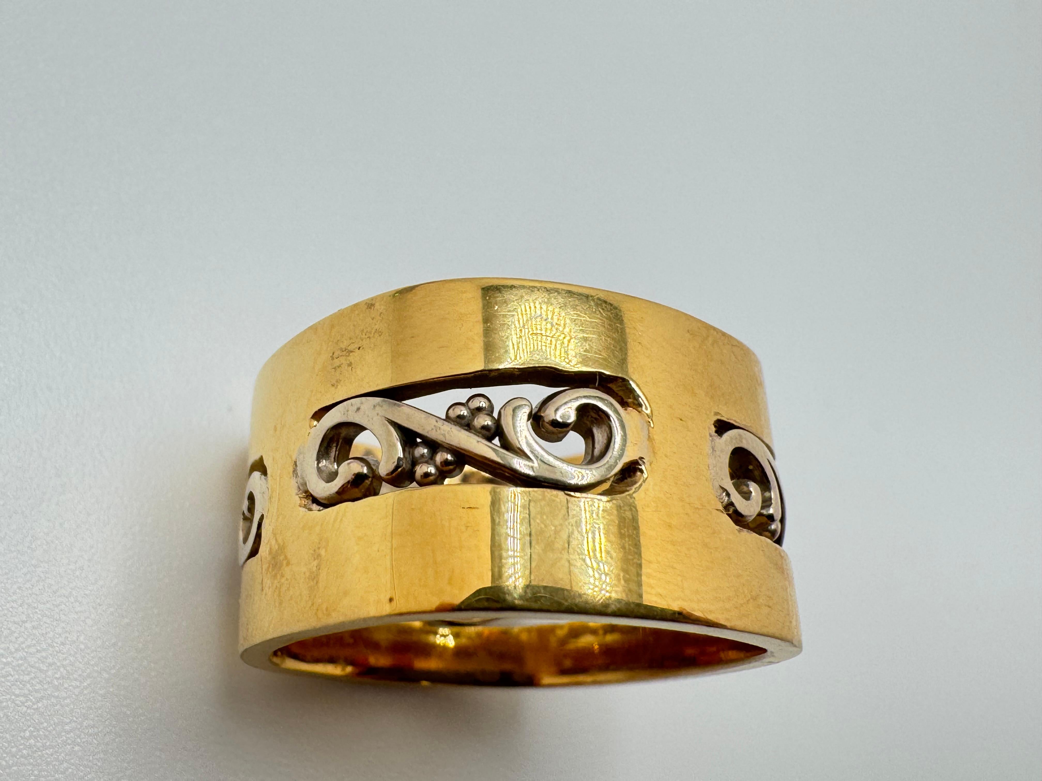 Questo elegante bracciale da donna è realizzato in oro 14K bicolore e unisce un design classico a dettagli raffinati. La fascia squadrata in oro giallo fornisce una base audace e contemporanea, mentre un delicato motivo a volute in oro bianco