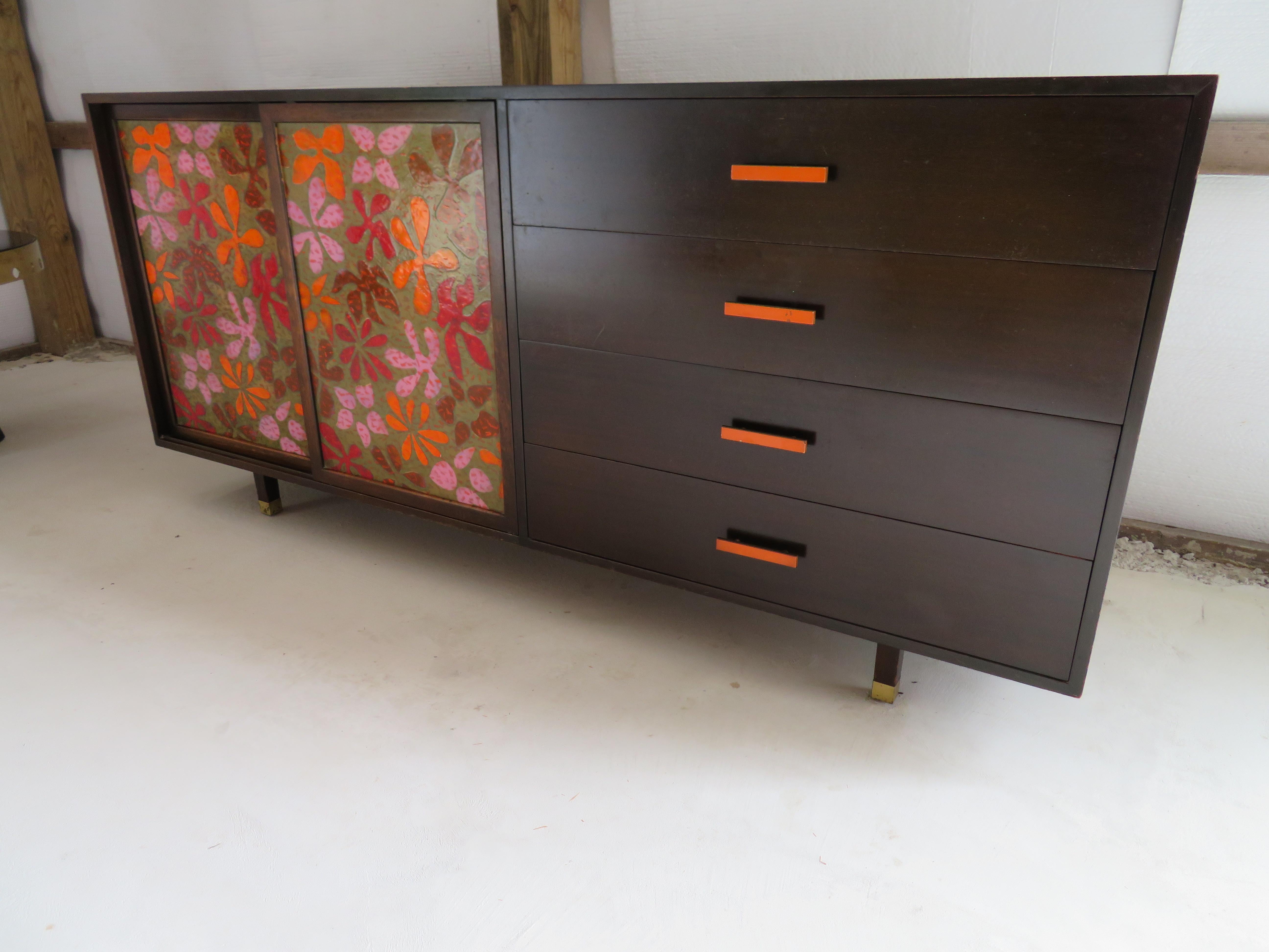 Cabinet or dresser featuring inset high-fired enamel-on-copper doors with a richly colored floral decorative motif. Dark mahogany case with brass pulls and sabots; white-lacquered interior drawer fronts. Solid secondary woods and dovetail joint