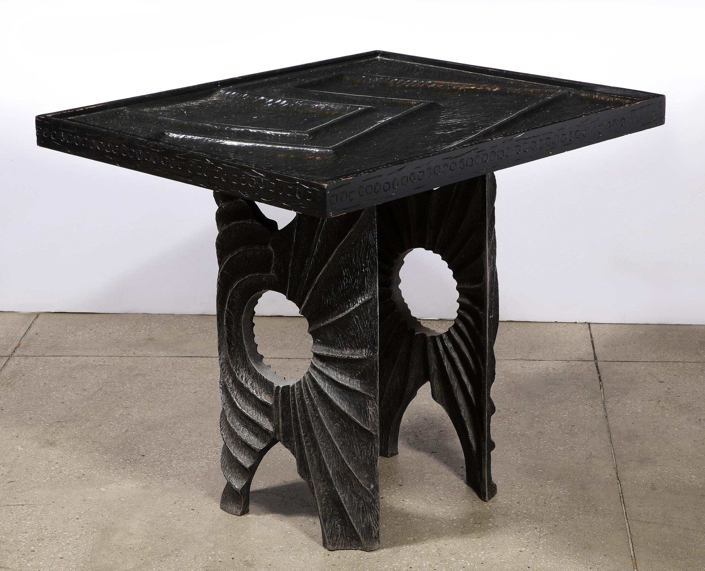 The unique sculpted aluminum table with abstract geometric chasing, supporting a black lacquered carved wood top.