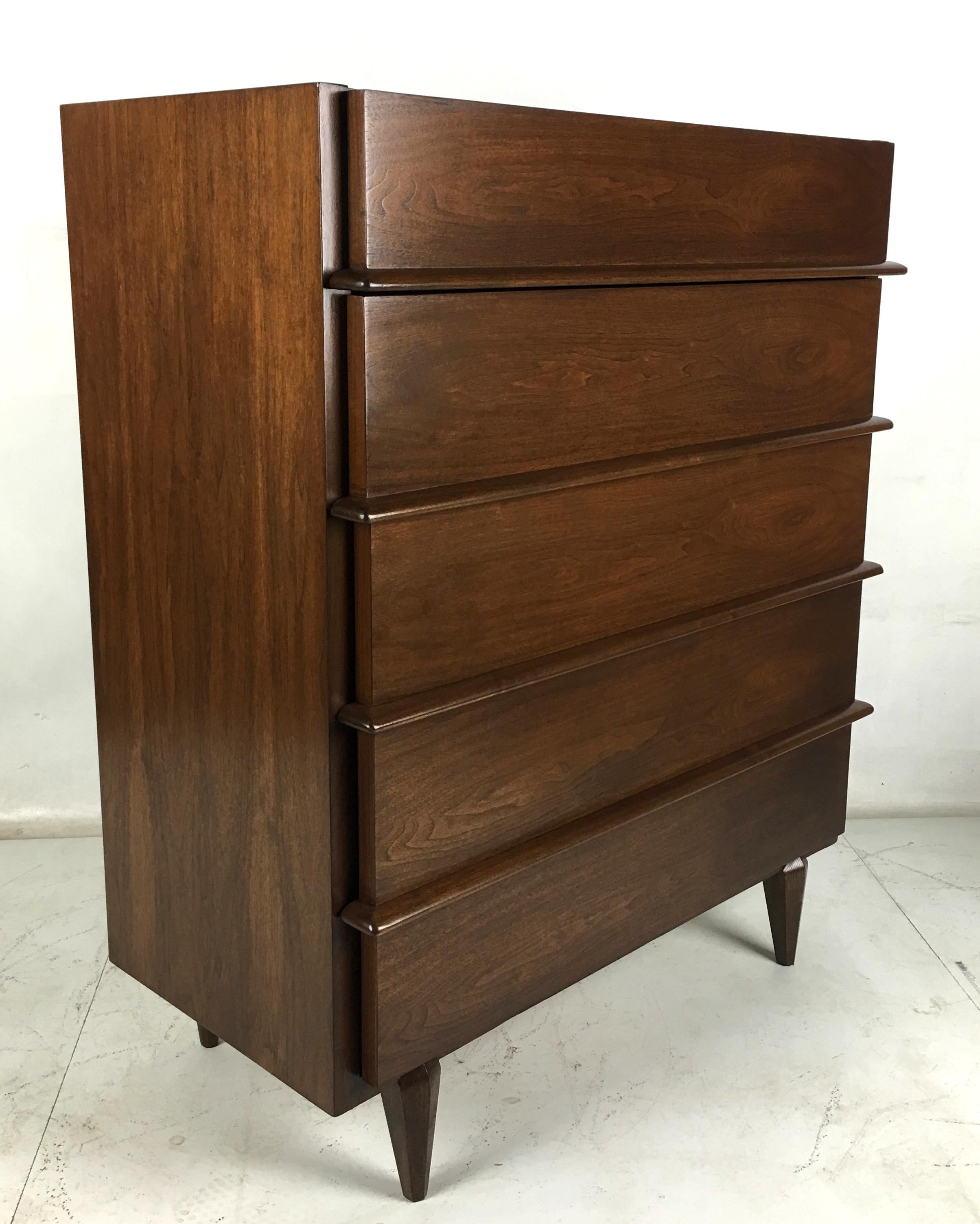 Walnut Highboy with full length sculpted drawer pulls by Merton Gershun. The drawers have beautiful graining and are given added dimension by the wraparound sculpted wood pulls.  The center-beveled, tapering legs are mounted forward of the apron,