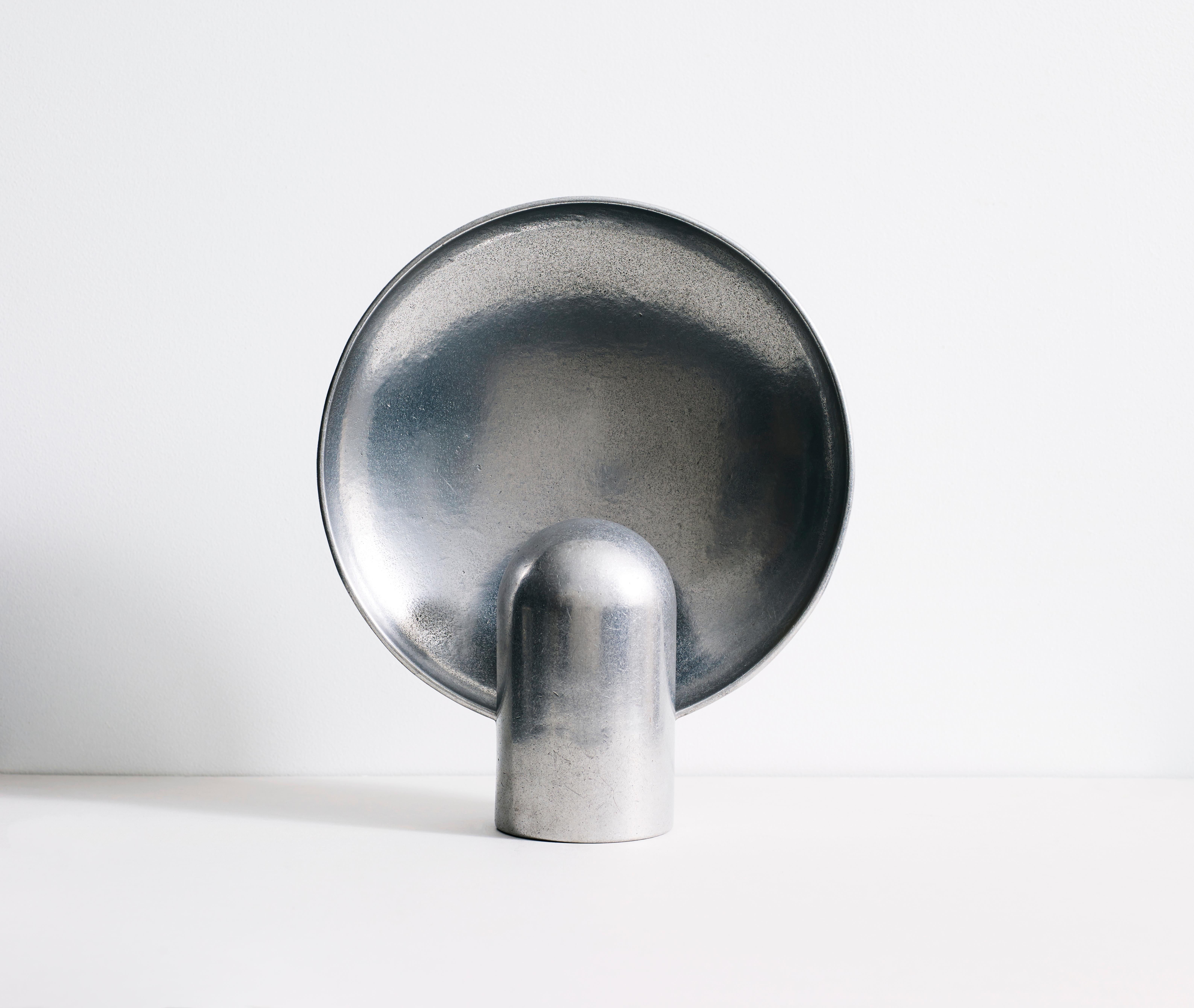 Sculpted lamp by Henry Wilson
Material: Aluminium, also available in different stones and bronze.

The surface sconce is an ambient, sculptural light cast in two halves from solid gunmetal. The casting is rumble finished for a smooth texture.

Each