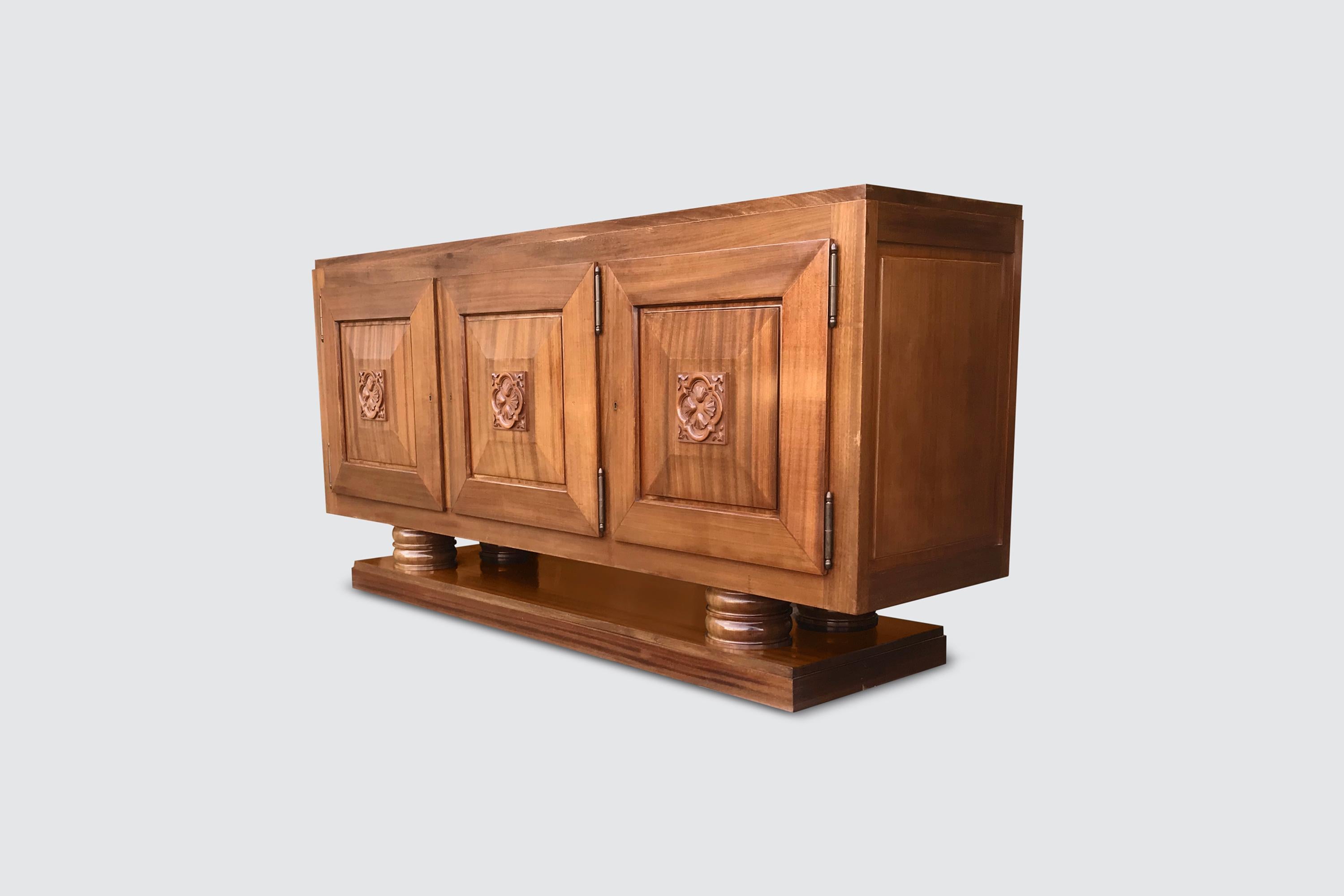 Beautifully sculpted art deco credenza by Gaston Poisson in solid mahogany wood.

The design is characterized by 2 round columns on each side that provides for a floating effect of the upper body. Interestingly offset against the bulky body, the