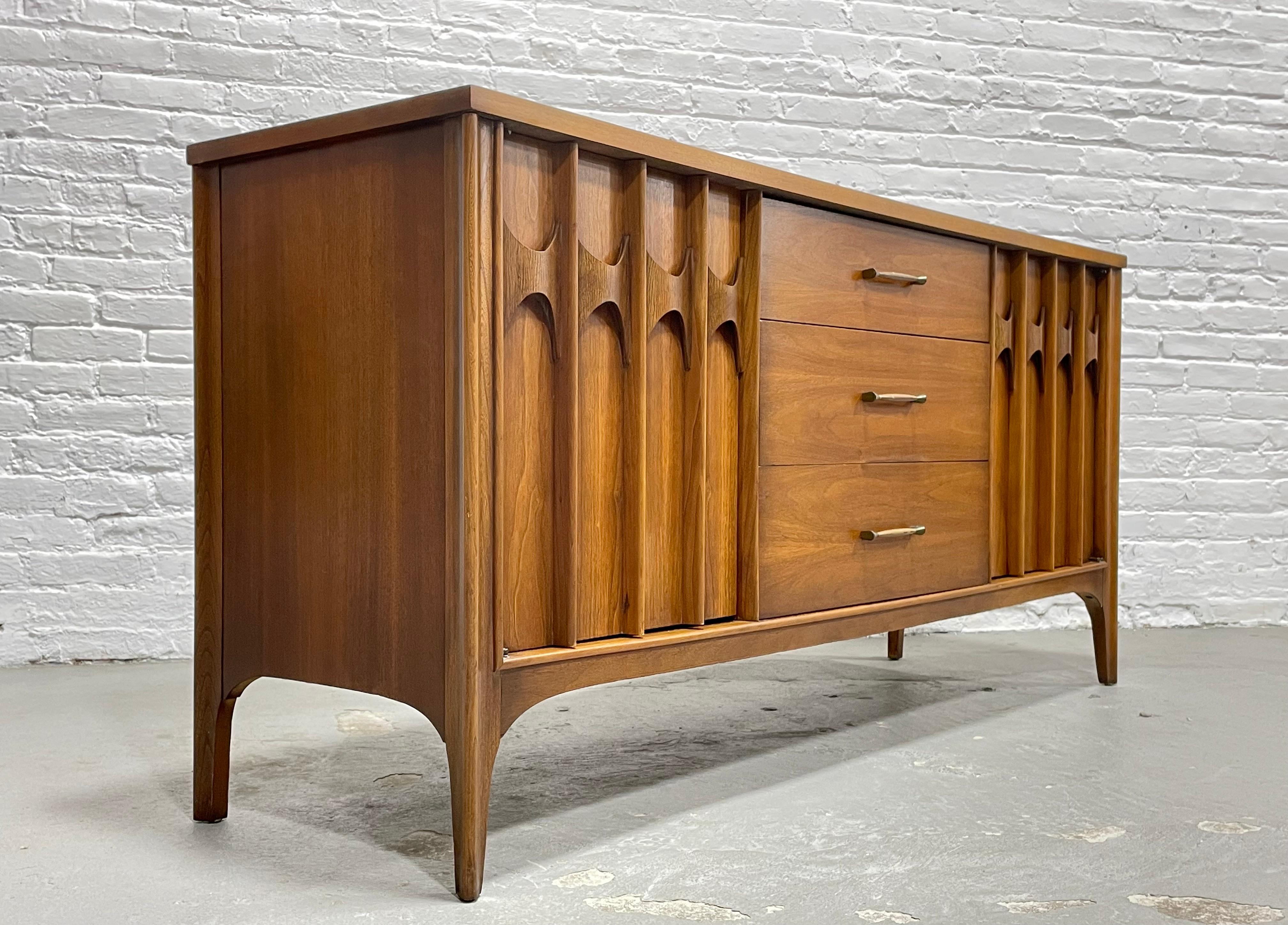 Sculpted Mid Century Modern Credenza / Long Dresser by Kent Coffey's Perspecta line, c. 1960's. This fabulous piece features three deep and spacious drawers at the center and a shelving area along either side. The credenza is crafted from gorgeous