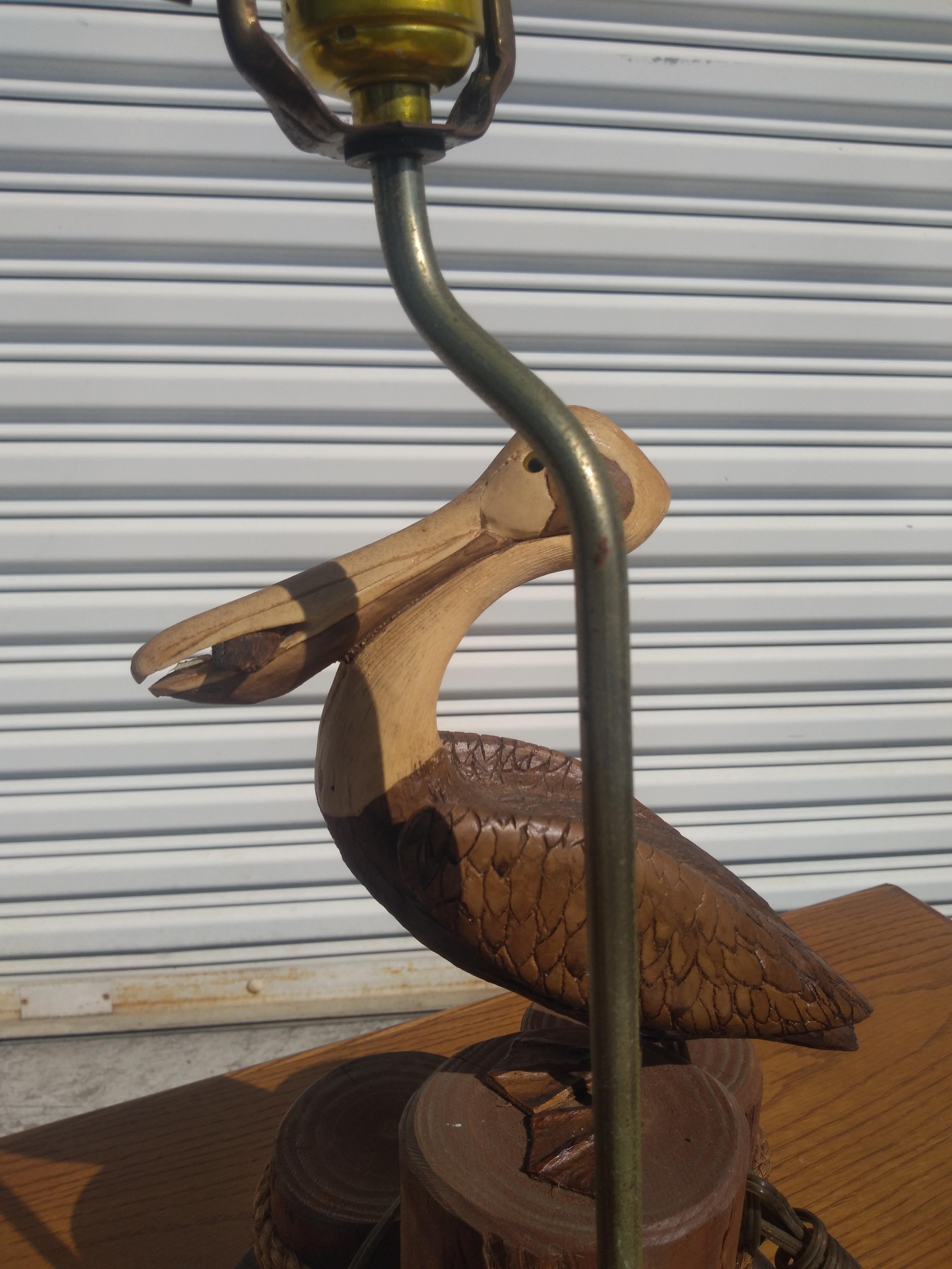 This lamp is folk art. It depicts a pelican on a wharf. Its base is a slab of o tree with 3 cut limbs depicting a wharf. The wharf has ropes and nets and a finely carved pelican sitting on the wharf. The pelican is painted and lacquered.

This lamp