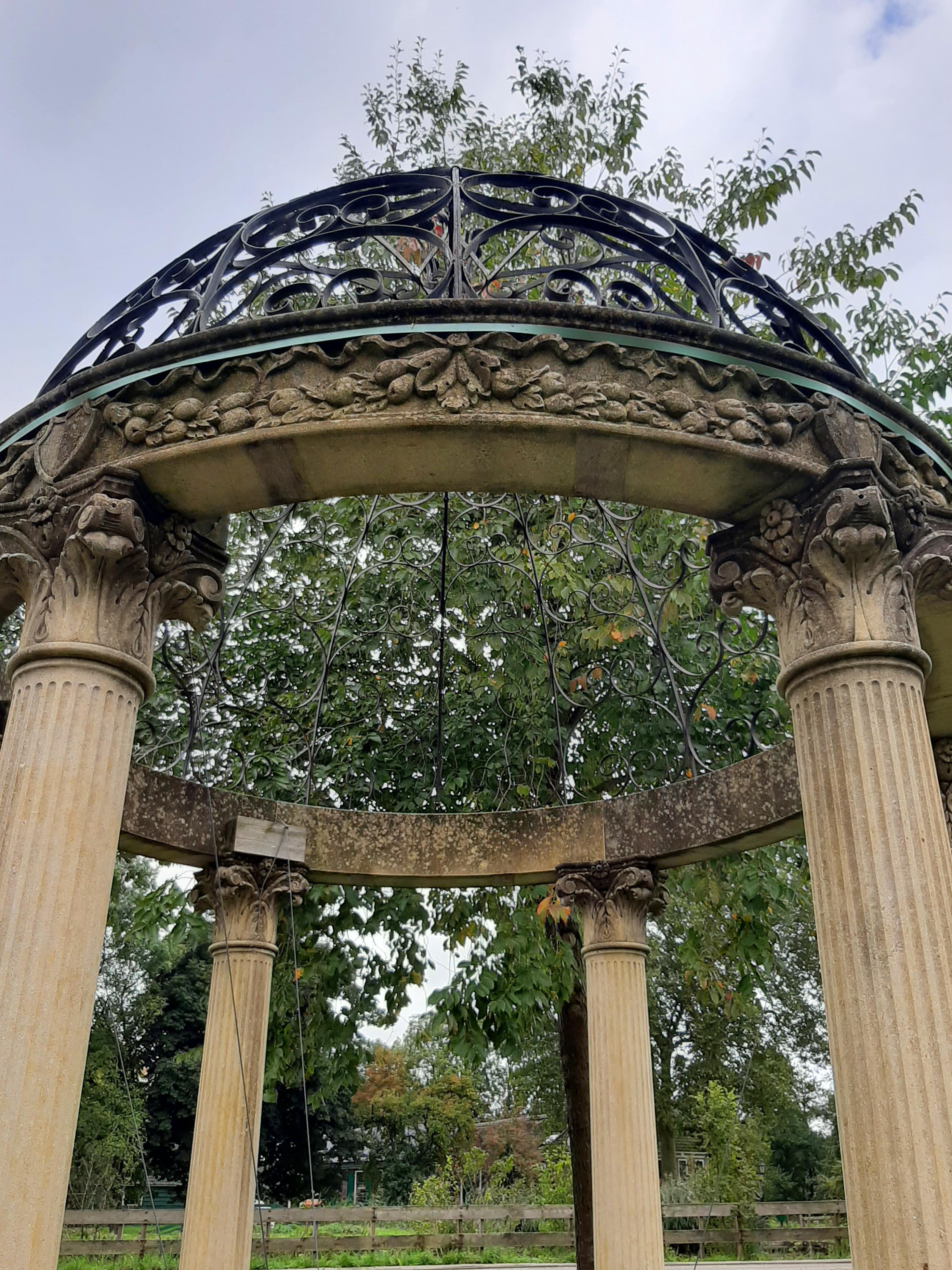 Sculpted limestone rotonda or garden gloriette in classical style with a wrought iron dome. Made in the early 20th century. The Rotonda has six fluted columns and benches with scrolled feet in between them. The pillars are carved in a classical