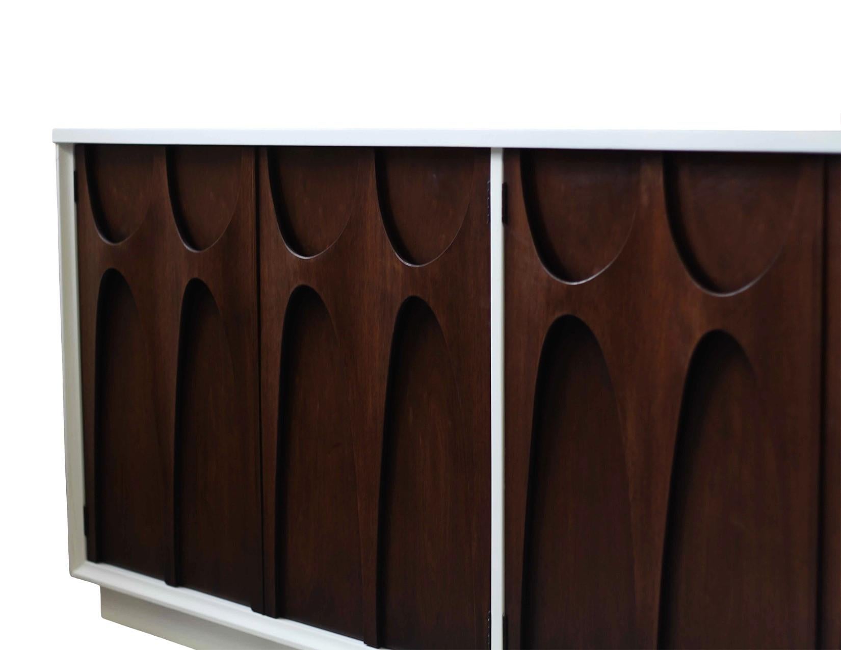 Two-toned Broyhill Brasilia Mid-Century Modern sculpted walnut credenza/sideboard. It features white lacquered exterior with a gorgeous dark stained walnut wood front, with sculpted arches and original pulls. It offers ample room for storage with