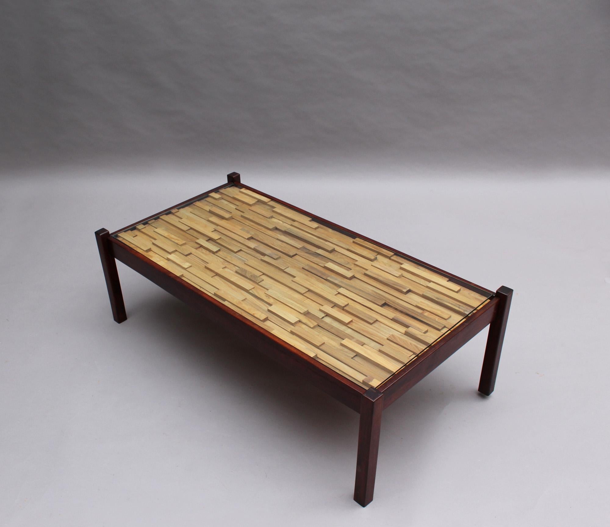 A mid-century Brutalist style coffee table with a staggered wooden block relief design, protected with a glass top.