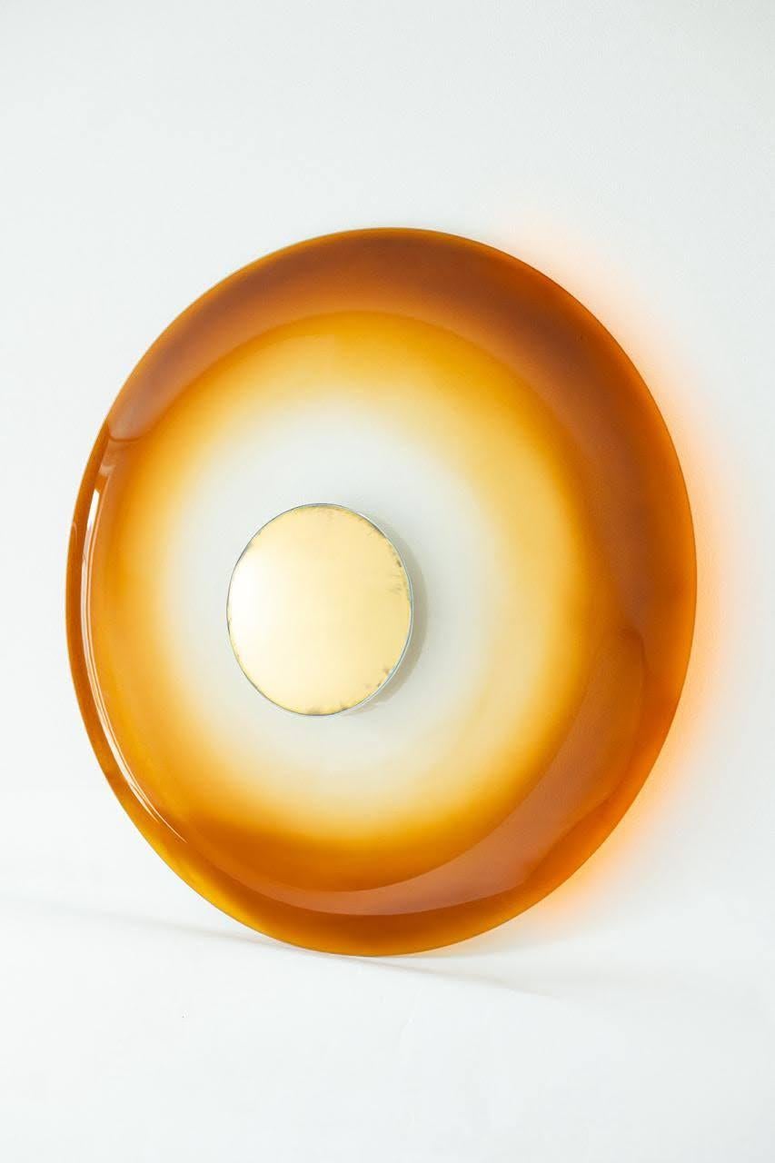 Ce miroir de la série Ikonika de MikusGlass est une fusion de techniques anciennes et modernes : un anneau extérieur en verre ambré lumineux, courbé au four, se transforme en un captivant miroir convexe en or, doré à la main selon la méthode rare de