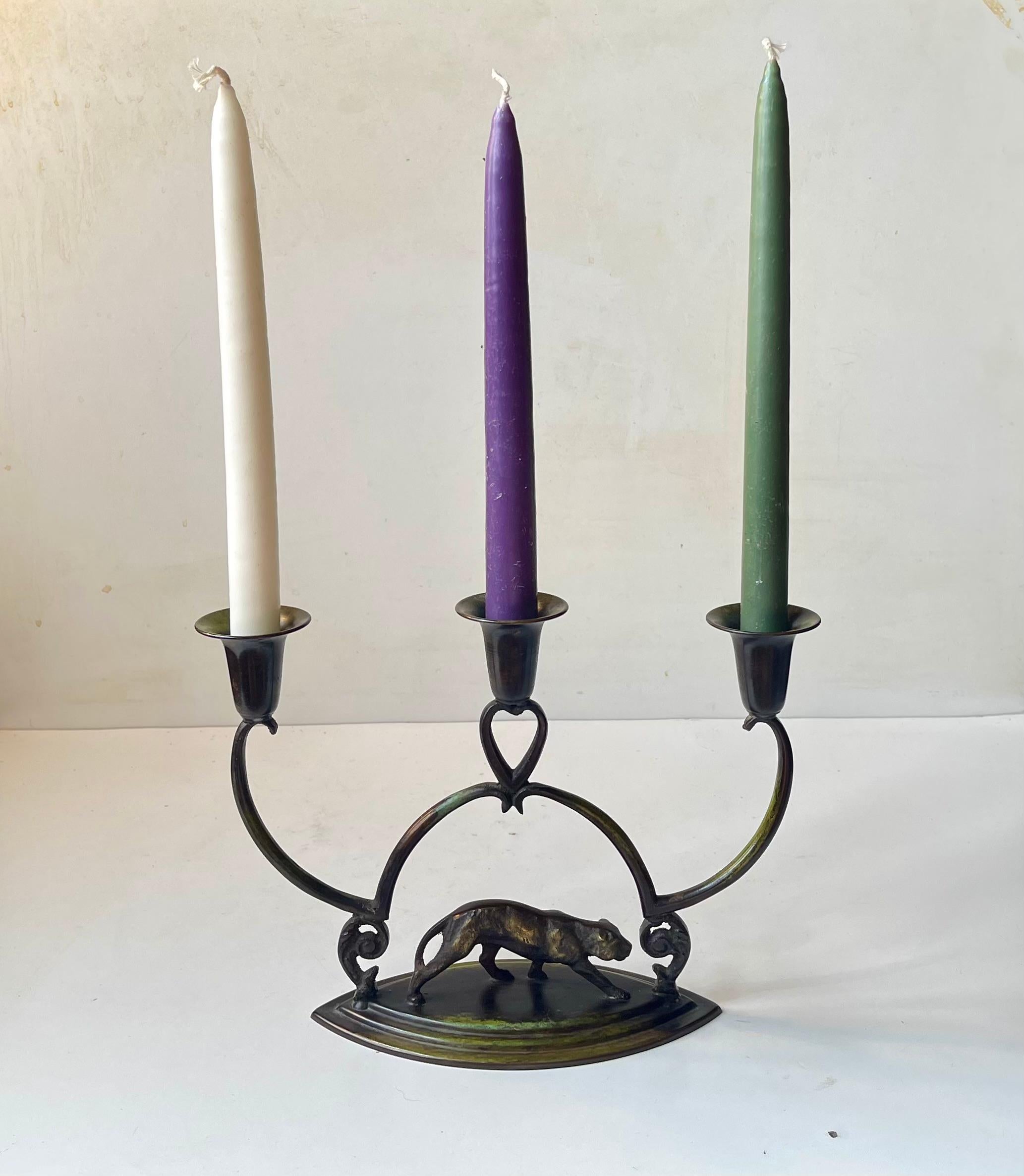 A stylized art deco candleholder for 3 regular sized candles. It features an architecturally 'staired' eye-shaped base and a center panther figurine to its base. 

Measurements: H: 20 cm, W: 27 cm, Dept: 9 cm.