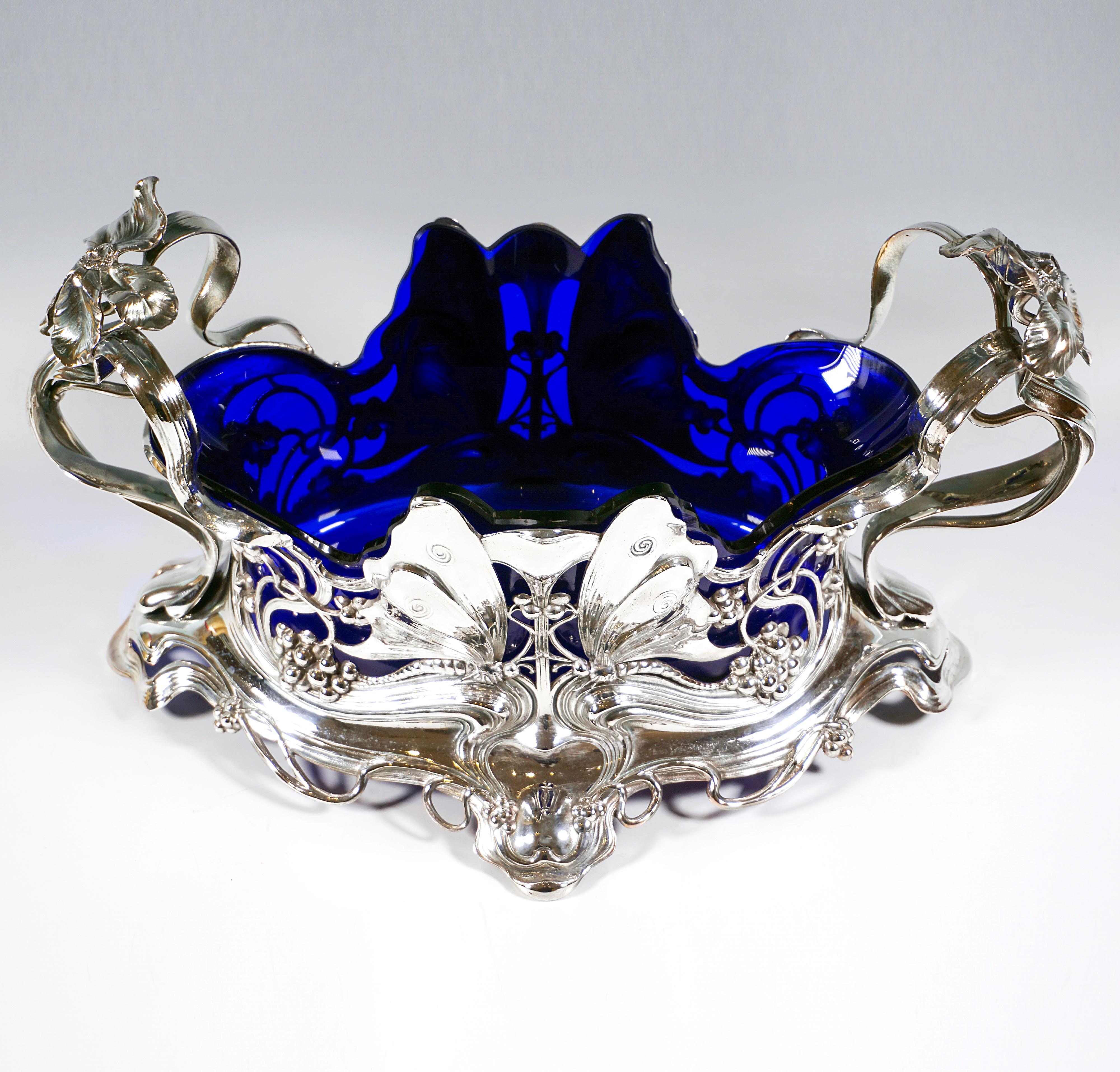 Elaborately designed vessel in an oval base shape standing on four cantilevered feet, openwork wall with symmetrically laid ribbons, bows and tendrils with berries, playing around two pairs of butterflies, towering, ‘flying’ bows form handles, each