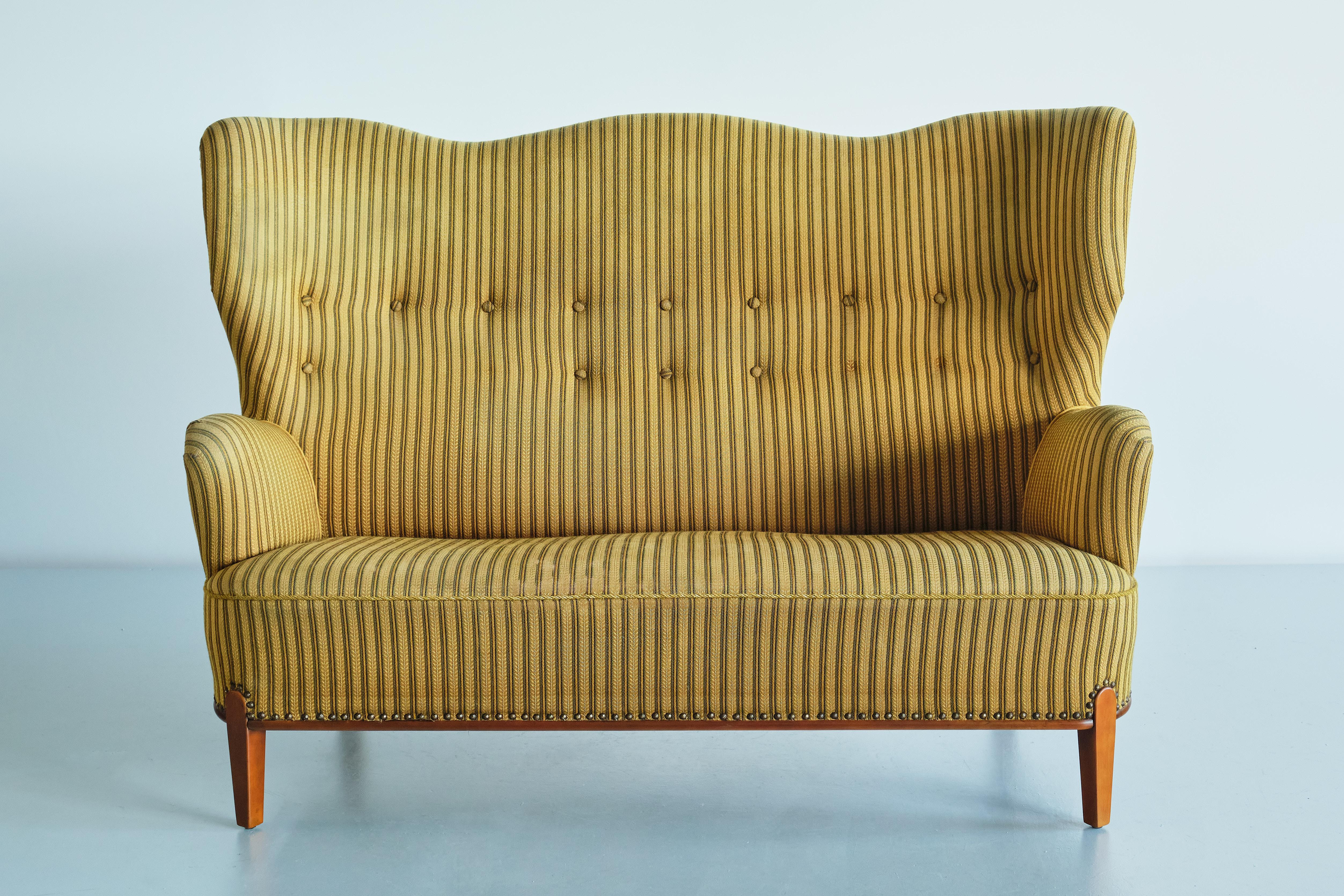 This sculptural sofa was designed by Bertil Söderberg and produced by Nordiska Kompaniet in Sweden in the 1940s. The rare design is marked by the curved lines of the buttoned back rest, ending in wing shaped sides and upholstered arm rests. A