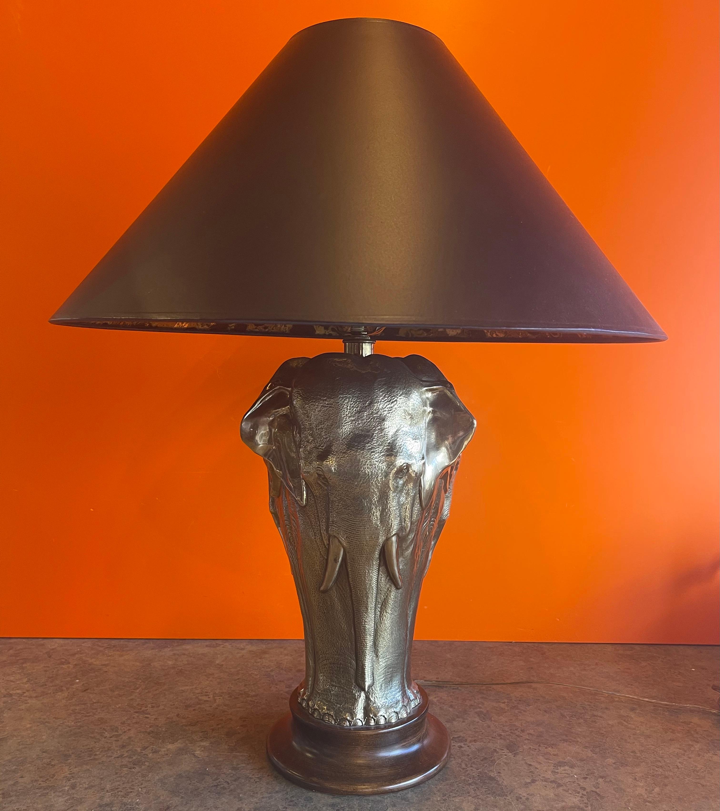 Gorgeous sculptural brass elephant table lamp on round wood base by Tyndale for Frederick Cooper Lamp Co. of Chicago, circa 1970s. The lamp features a brass elephant repeated equally around wood base with the original black shade signed 