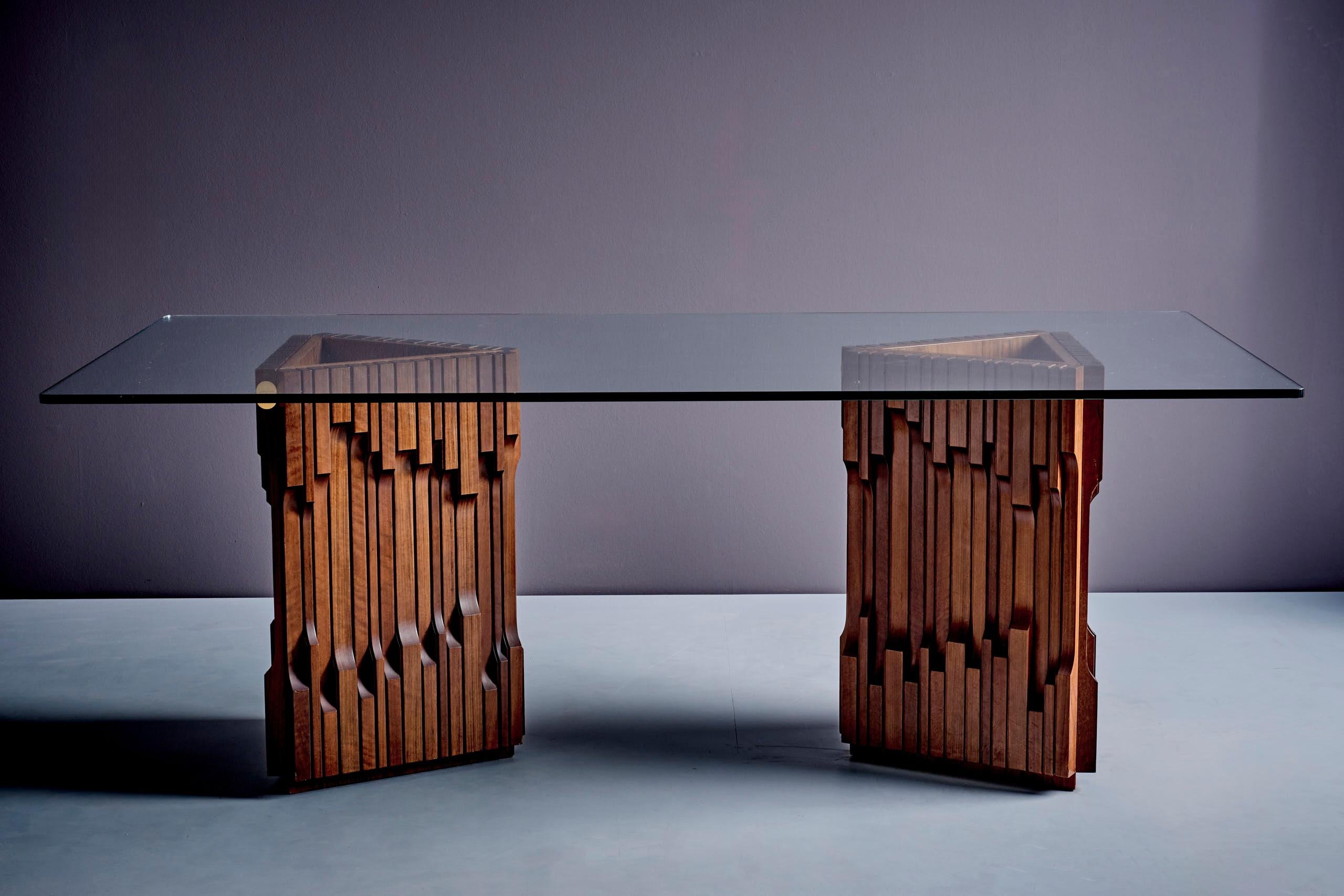 A striking and rare dining table designed by Luciano Frigerio, featuring two intricately carved solid wood pedestals that serve as both structural support and artistic statement. The geometric and sculptural bases showcase Frigerio’s signature