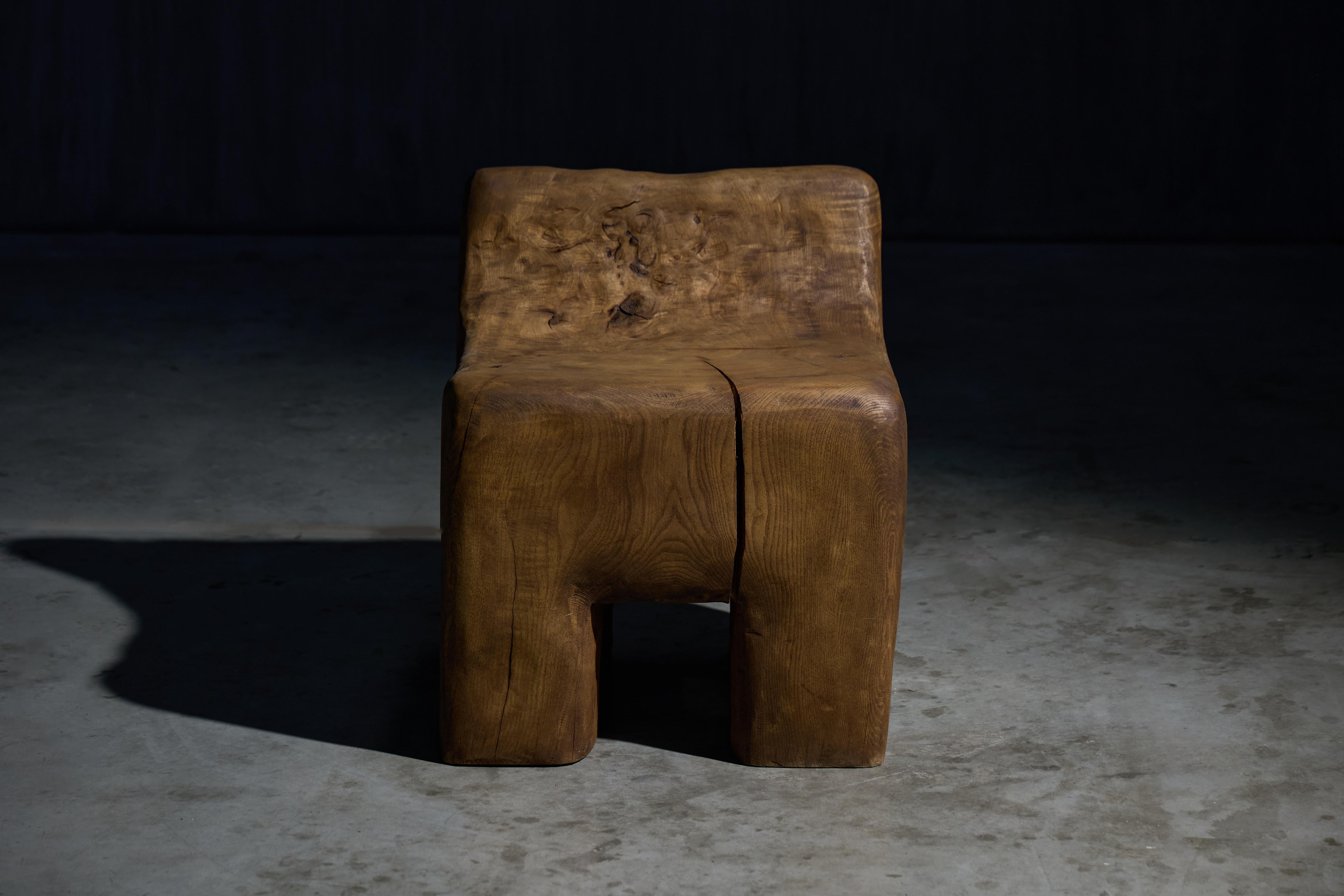 This sculptural side chair was crafted in 2024 from reclaimed solid wood. Soft curves and gentle undulations form an ergonomic seat, while deep fissures and expressive grain patterns highlight the raw character of the material. Its low-slung profile