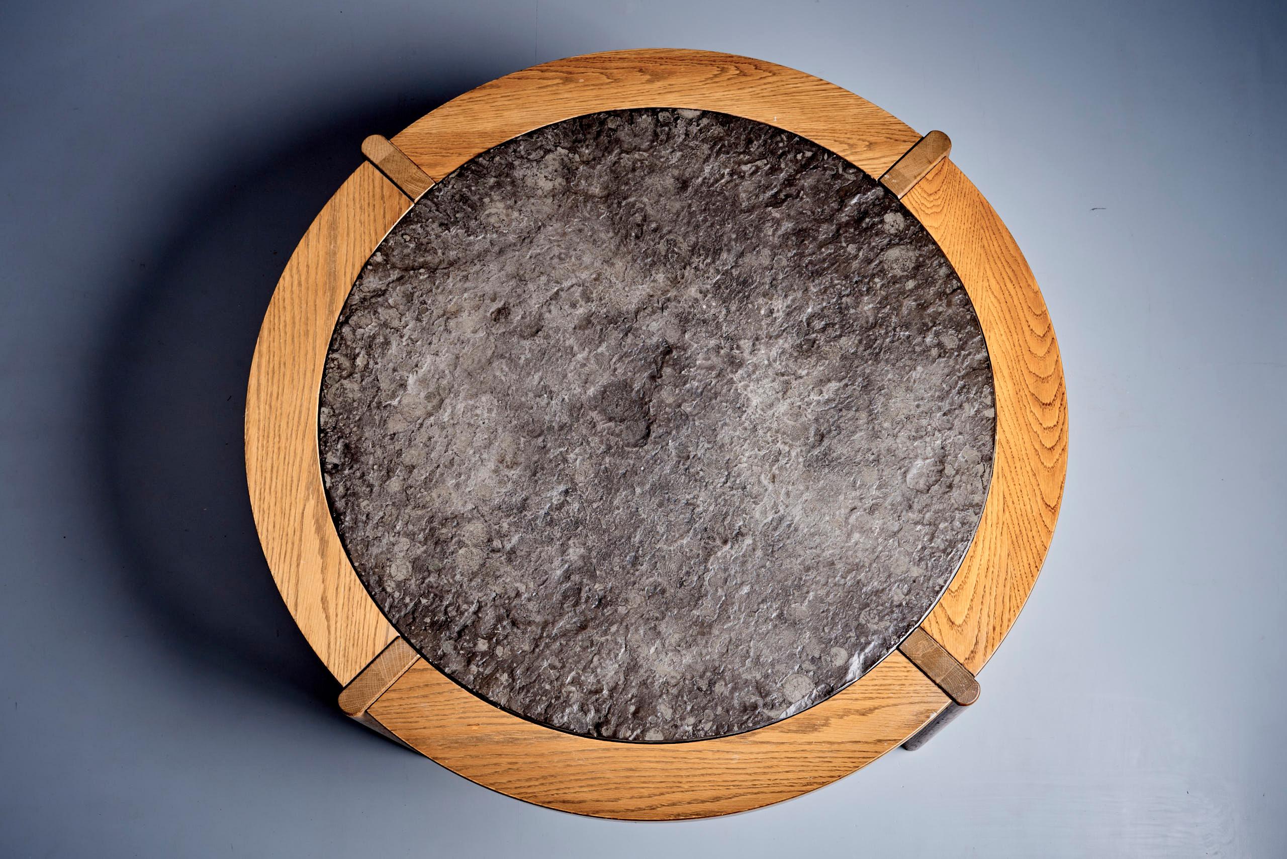 A standout piece of 1970s design, this collectible coffee table features a masterfully constructed solid oak frame with architectural joinery and a unique inset fossil stone top rich in natural textures and embedded fossils. The circular form is