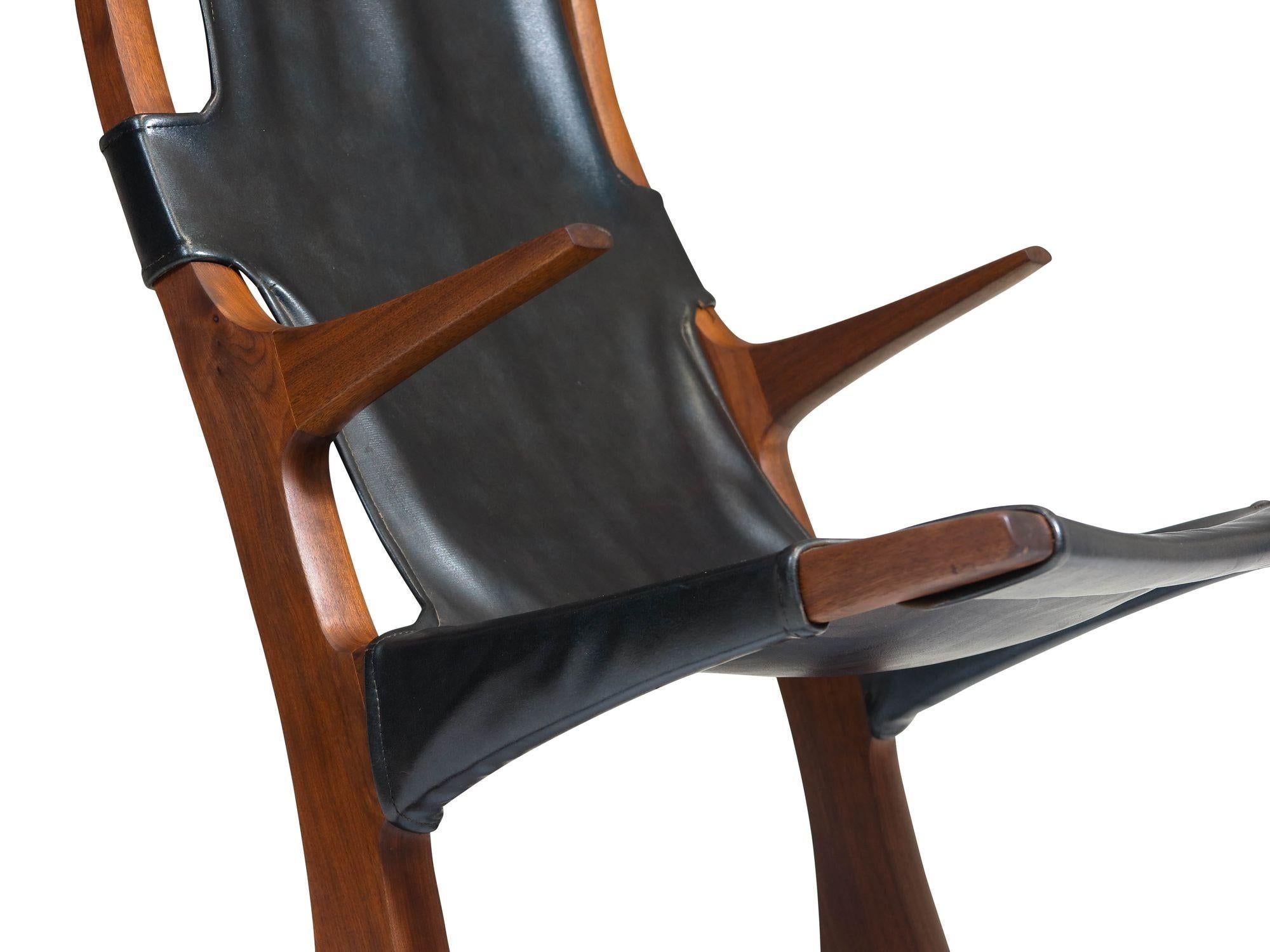 1970's California studio crafted rocking chair of solid black walnut with floating arms, and original black vinyl sling upholstery. Finely hand sculpted with exposed joinery, this stunning eye-catching piece blends artistry and