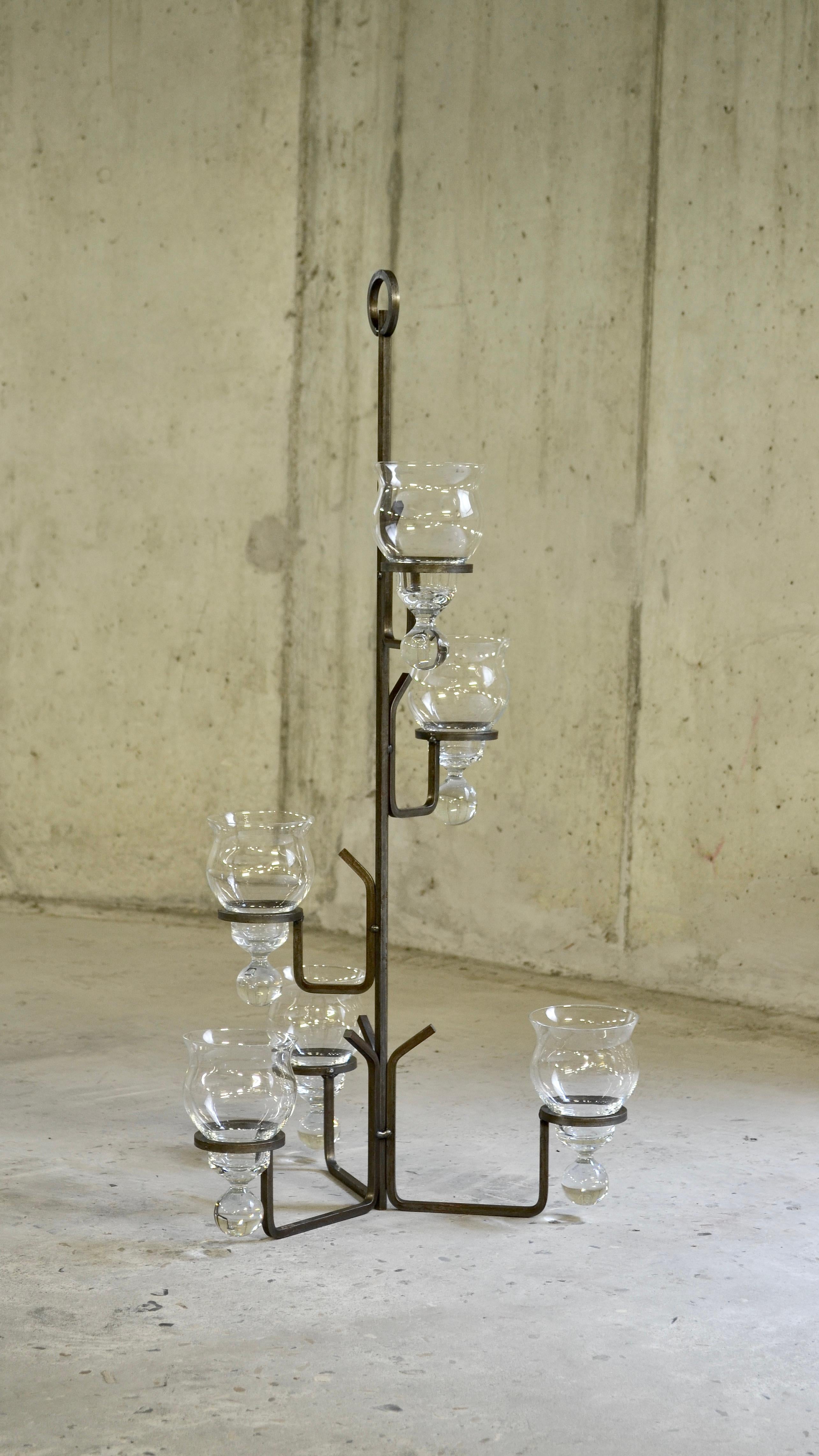 L'alleanza tra brutalismo e delicatezza.

La struttura curva in ferro battuto è collegata a barre sottili e inalterabili saldate tra loro. I candelabri di vetro, racchiusi in anelli di ferro, mostrano piccole gocce di vetro come se fossero congelate