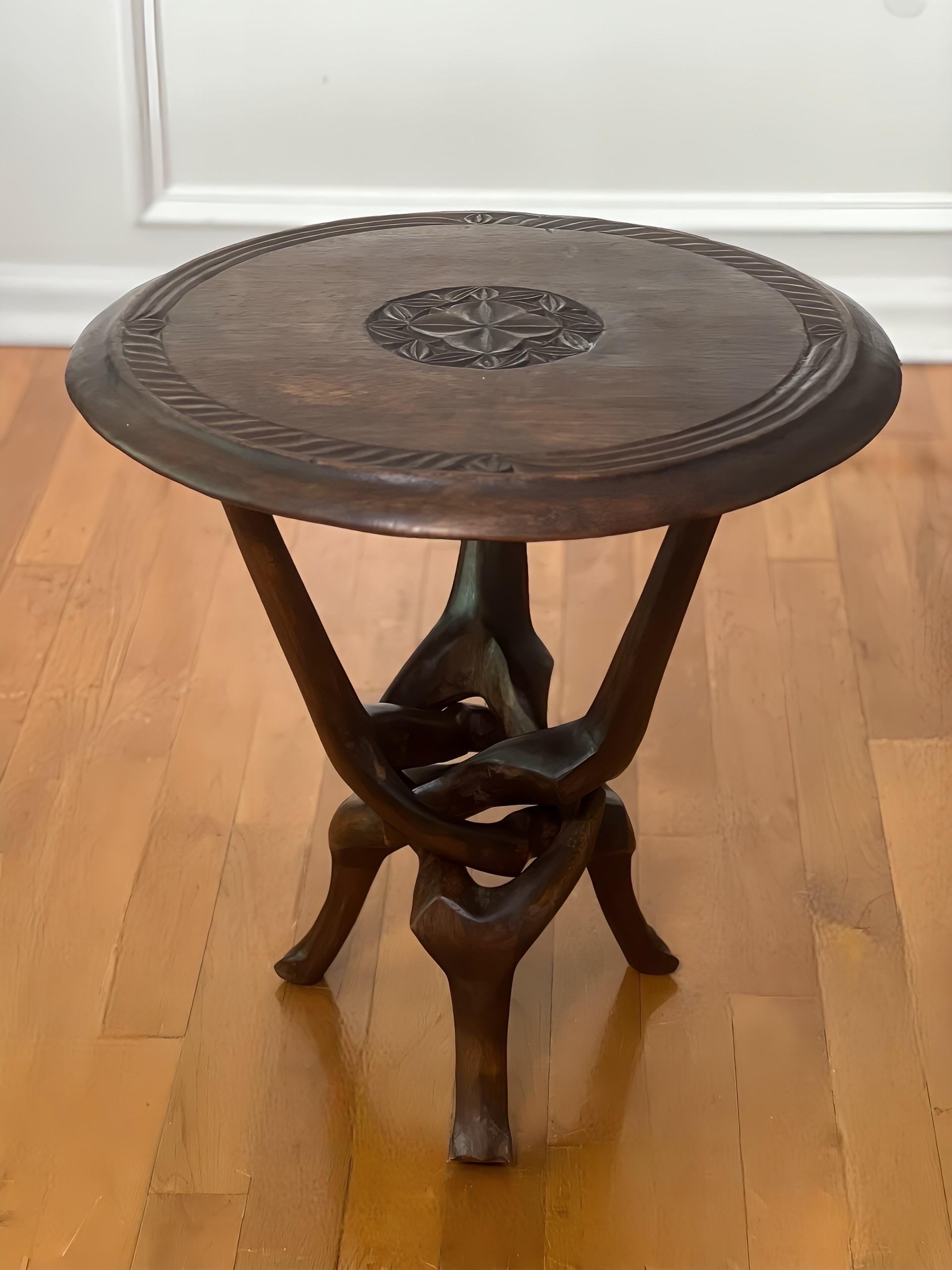 African sculptural carved hardwood side table with a collapsible tripod base, 1960s.  Handcrafted by a skilled artisan featuring an interlocking base sculpted from a single piece of smooth indigenous wood and a beautifully carved top with a center