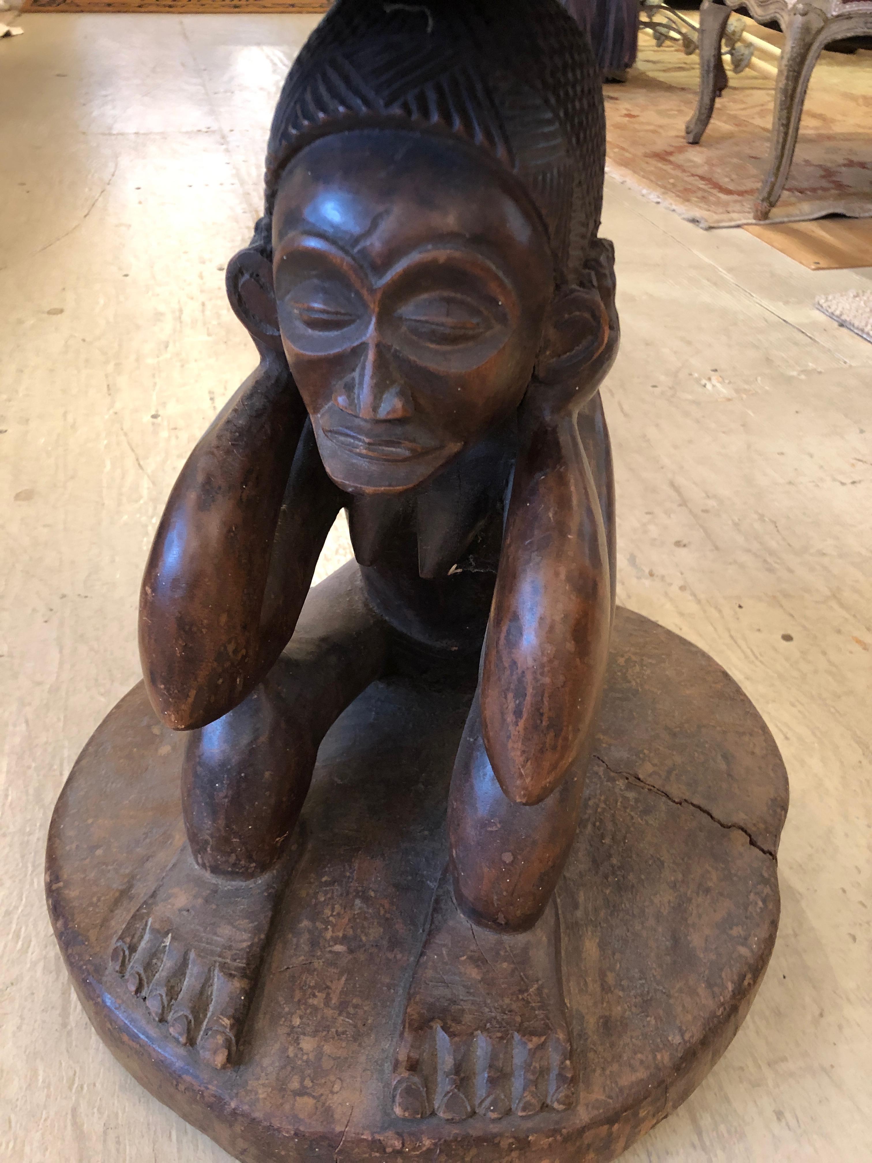 A handsome small round carved wood rustic side table or drinks table having a crouching figure with his hands over his ears as the sculptural base of a thick rustic tabletop.