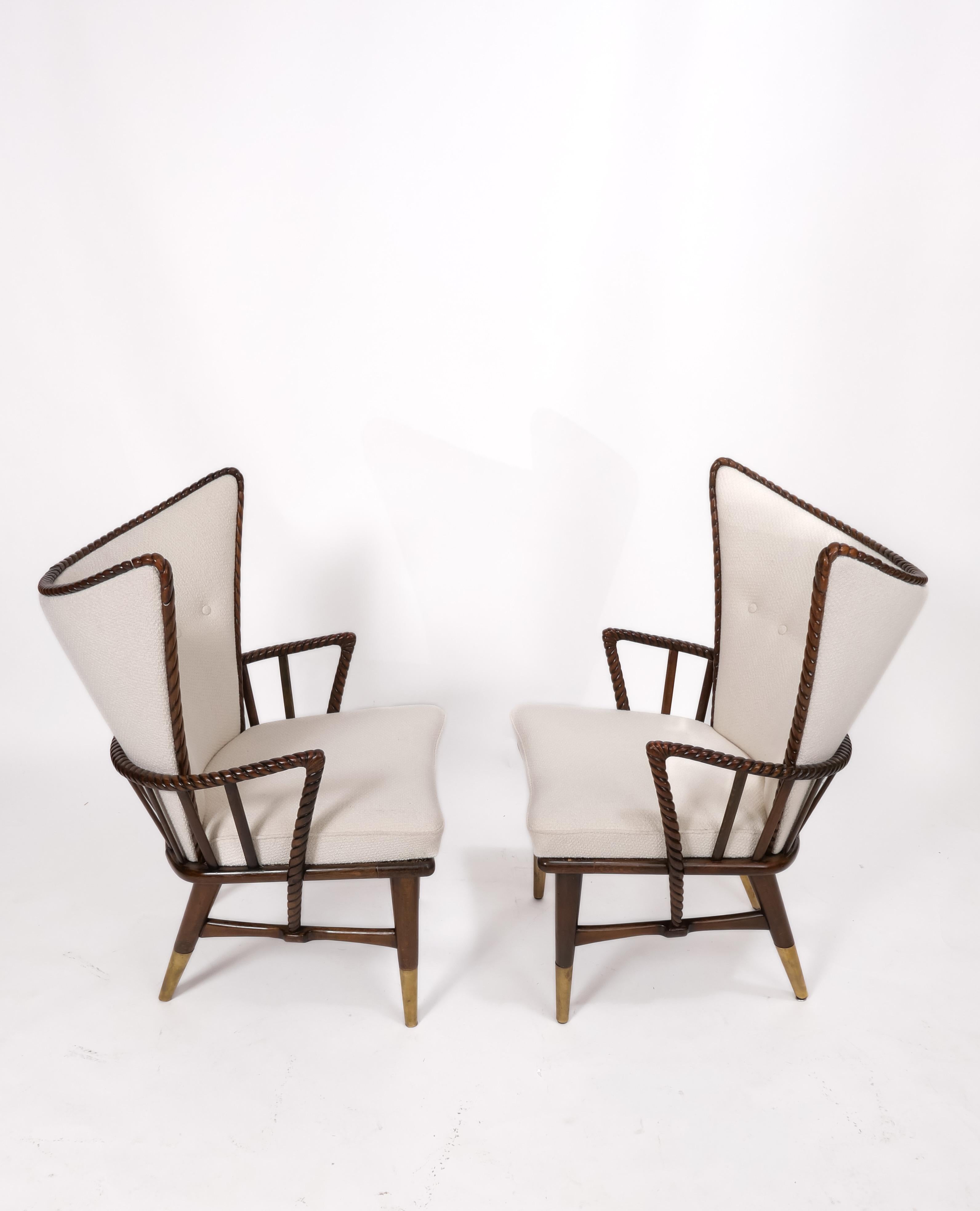 Dramatic winged armchairs feature intricately carved wood frames and brass boots. Maker unknown, recently imported from Europe and fully restored with a slightly nubby-textured ivory woven wool upholstery. Really elegant chairs. Beautiful from any