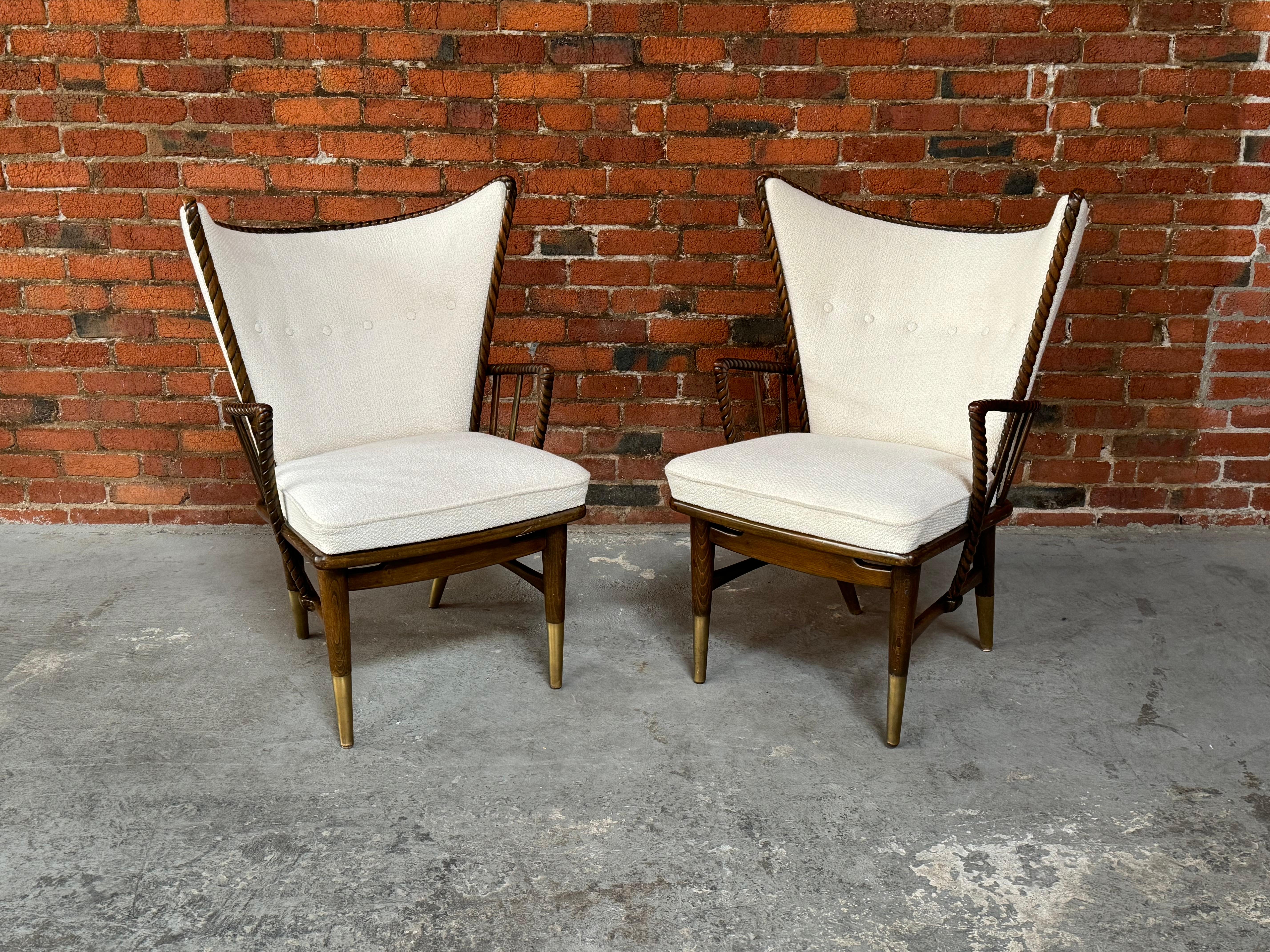 Dramatic winged armchairs feature intricately carved wood frames and brass boots. Maker unknown, recently imported from Europe and fully restored with a slightly nubby-textured ivory woven wool upholstery, with frames crafted out tropical hardwood.