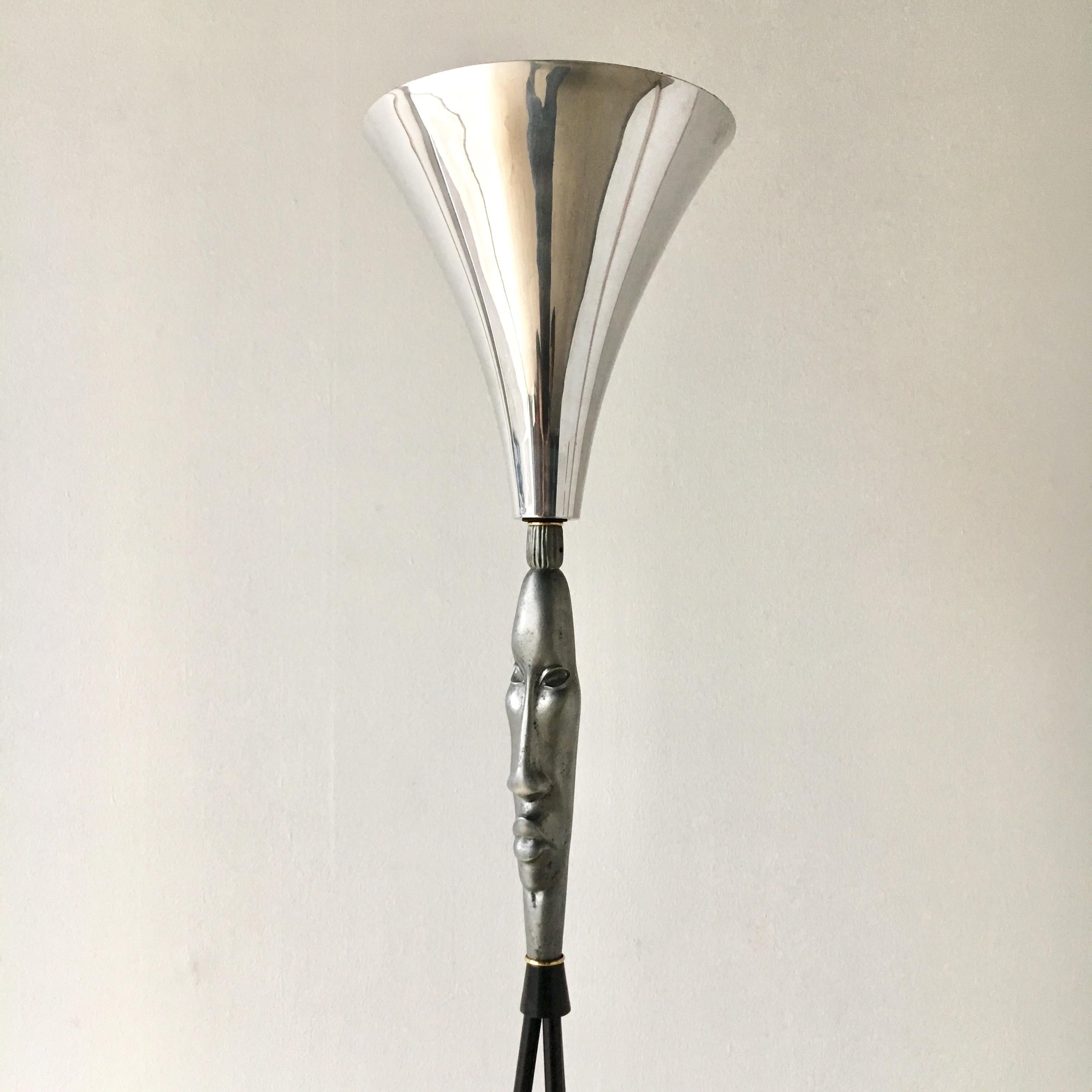 A sculptural cast aluminium uplighter floor lamp with a Tiki face supporting a polished aluminium conical shade and set on a blackened steel rod tripod base, on a circular steel base, 1940s.

There is light tarnishing to the aluminium but otherwise