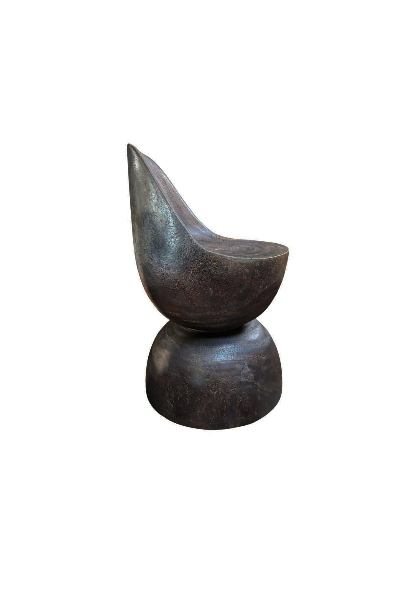 Dieser skulpturale Stuhl aus Suar-Holz, der fachmännisch aus einem einzigen, massiven Holzblock geschnitzt wurde, wertet Ihren Raum auf. Seine fließende, organische Form bringt die natürliche Krümmung und Maserung des Holzes zur Geltung, während das