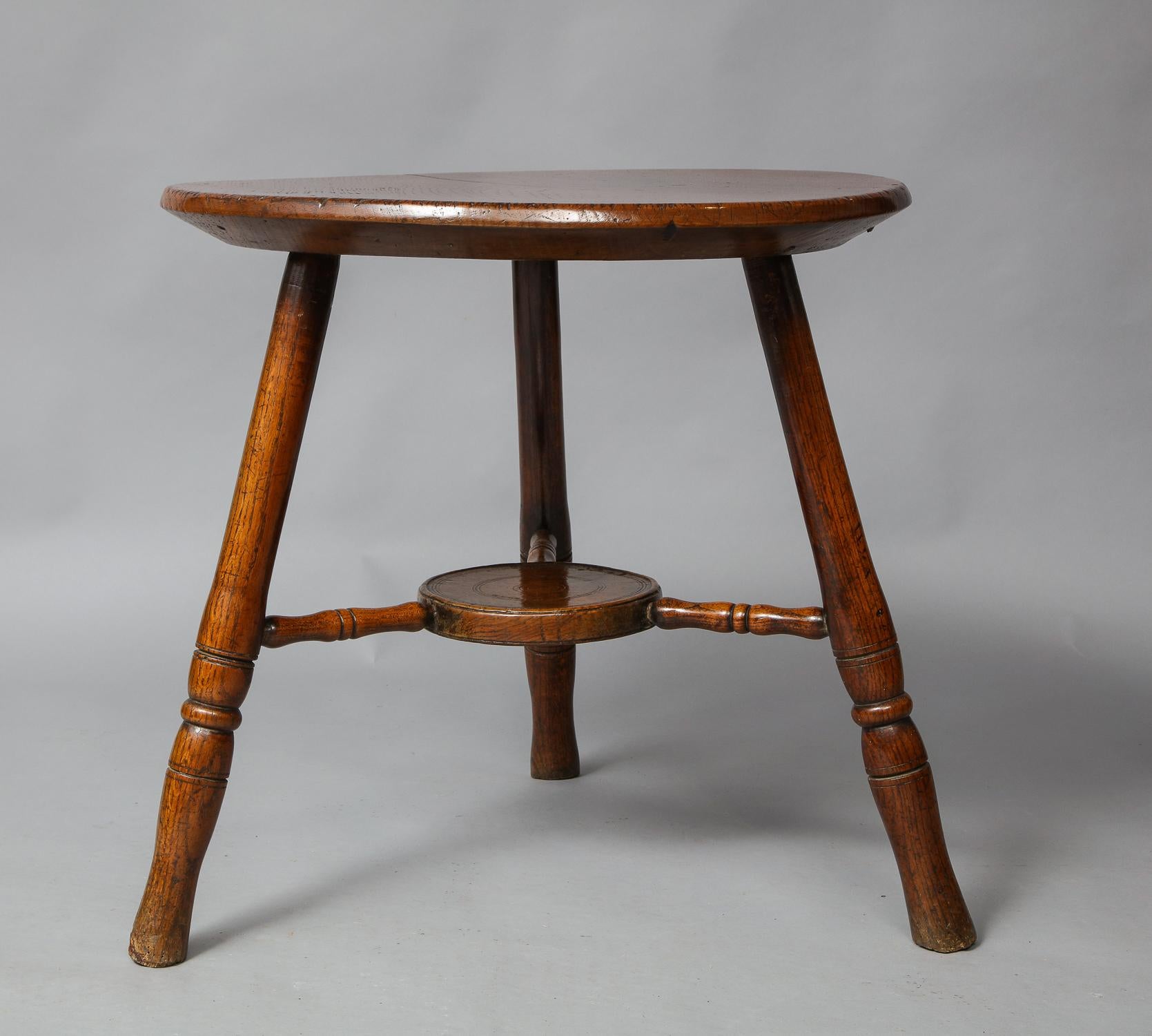 An early 19th century Welsh cheese-top cricket table featuring a thick chamfered top with great color and patina, and an unusual incised roundel undertier jointed by three turned stretchers, on well turned splayed legs. A sculptural and balanced