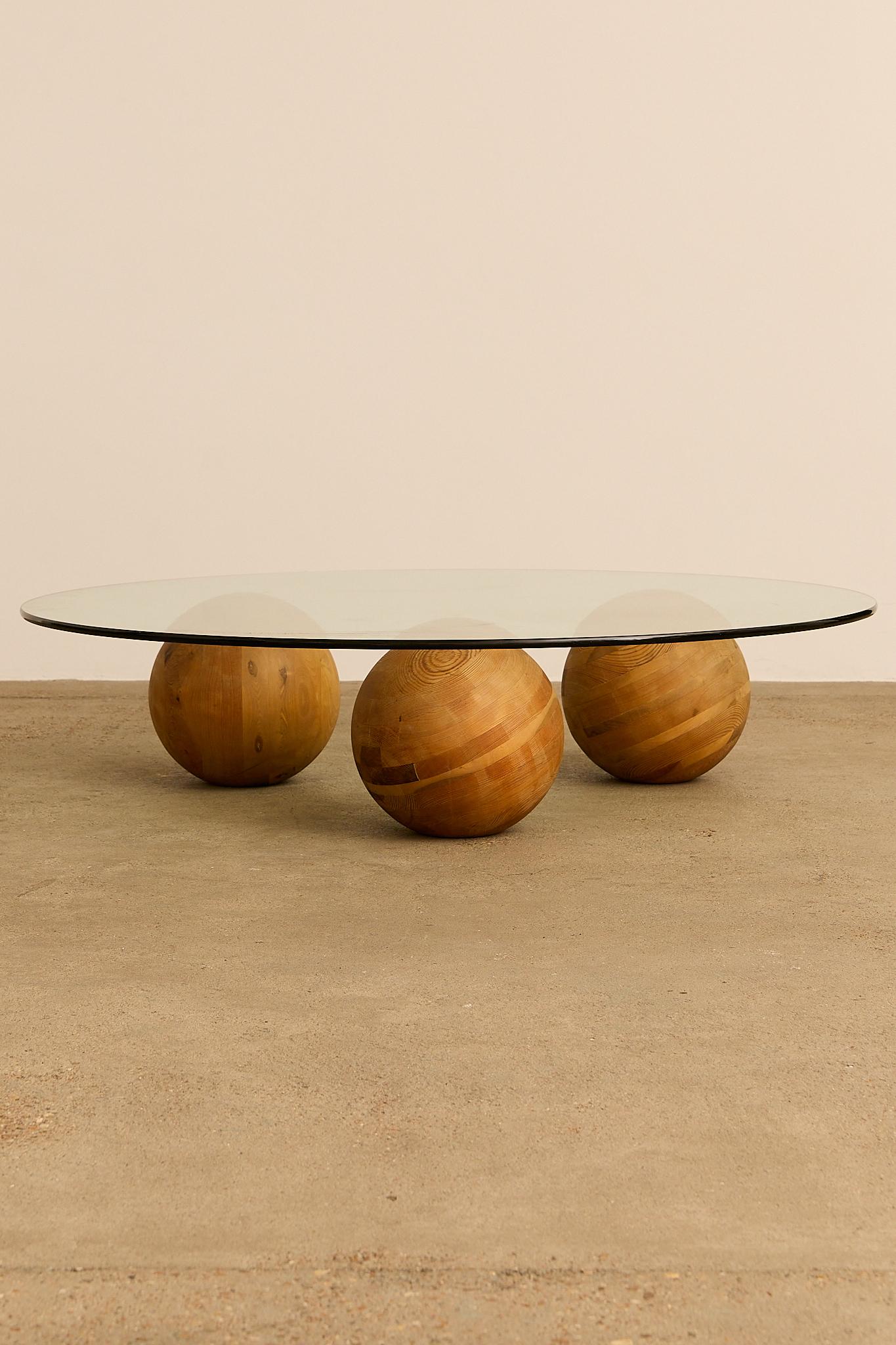 Mélange frappant de géométrie et de matériaux naturels, ce meuble présente un plateau de verre ovale et élégant reposant délicatement sur trois sphères en bois massif. Chaque sphère est fabriquée à partir d'un bois richement grainé, présentant des