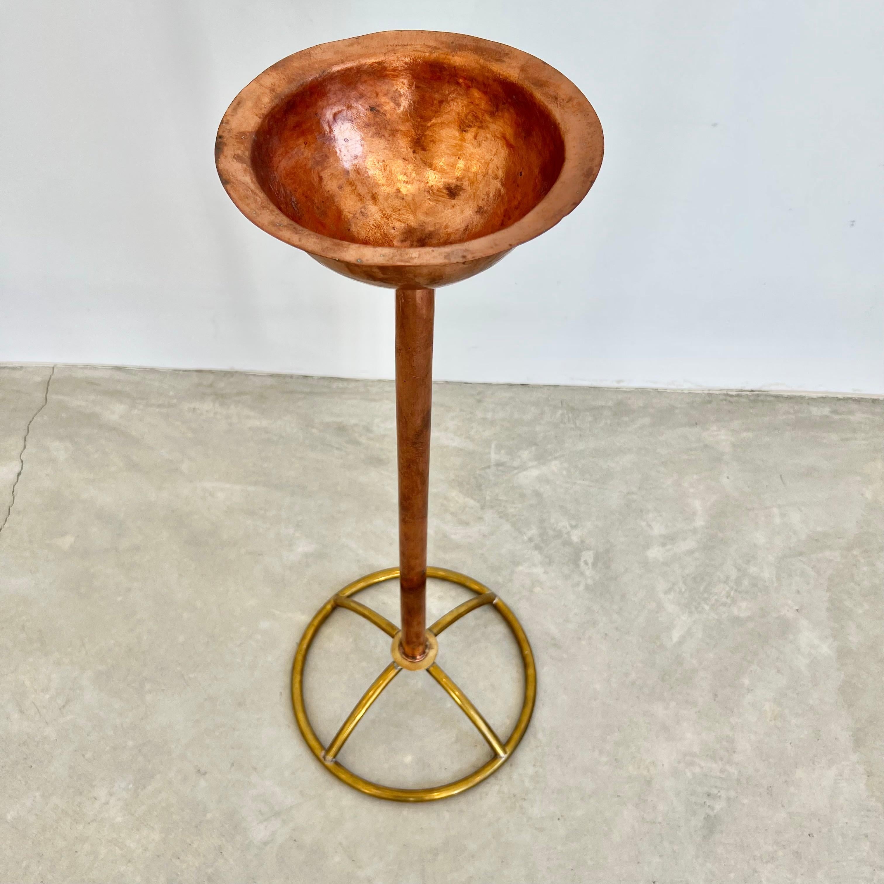 Sculptural standing catchall made of brass and copper. Large solid copper bowl with a thin rim floats atop a substantial copper rod. The copper body of the catchall is affixed to a beautiful round brass wheel base. Amazing brushed patina to copper