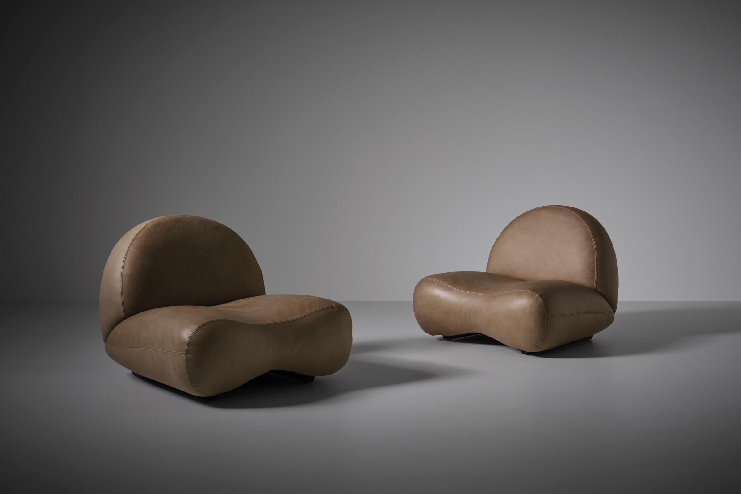 Sculptural curved leather lounge chairs, Italy, 1960s. Nice strong curved bulky shaped design upholstered in a high quality smooth light taupe / bone colored aniline leather. Beautiful from each angle; strong & masculine from the front side and