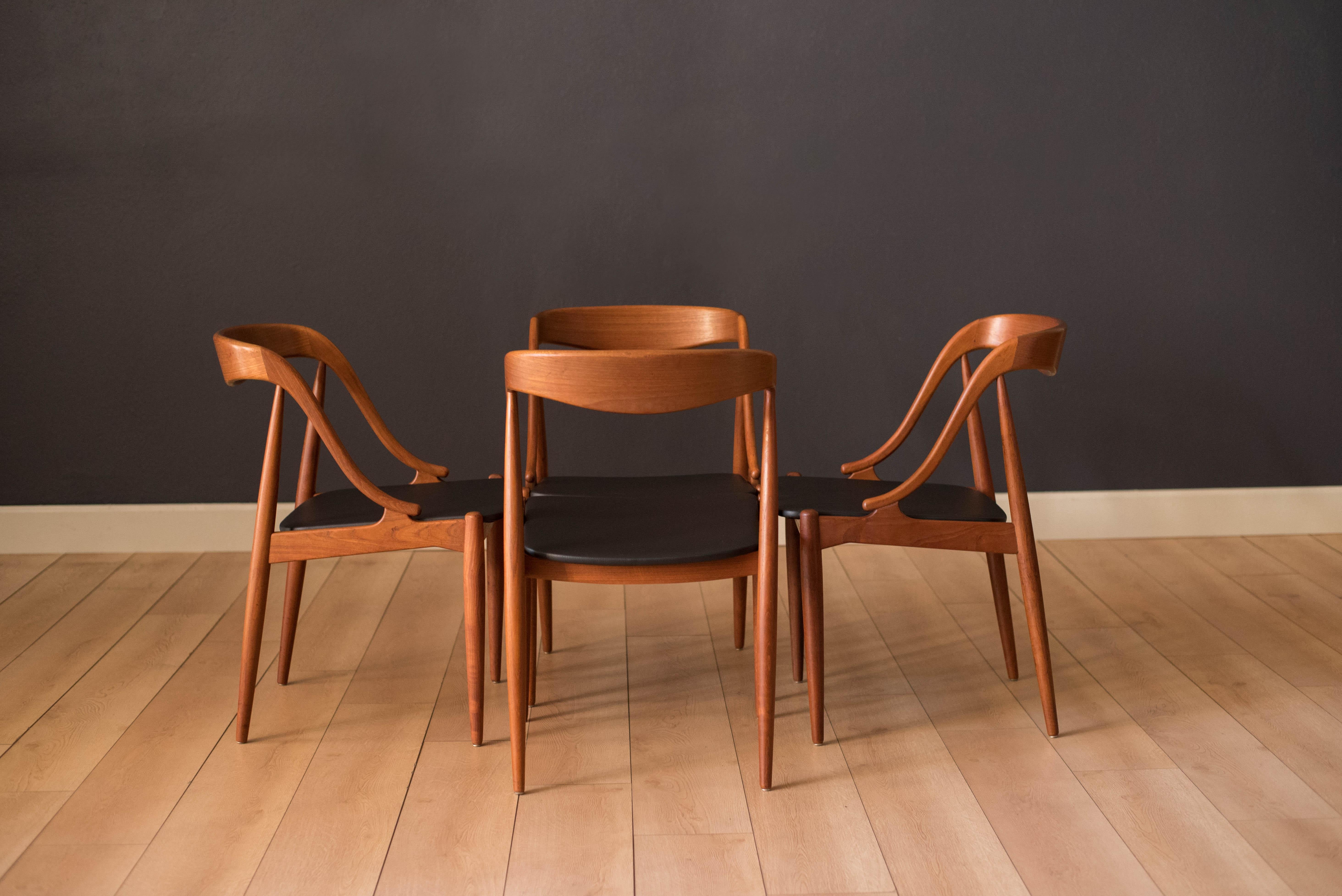 Mid-Century Modern teak dining chairs by Johannes Andersen for Uldum Mobelfabrik. This set includes four dining chairs with newly reupholstered black vinyl seats. Designed with curved backrests and sculptural teak frames. Price is for the