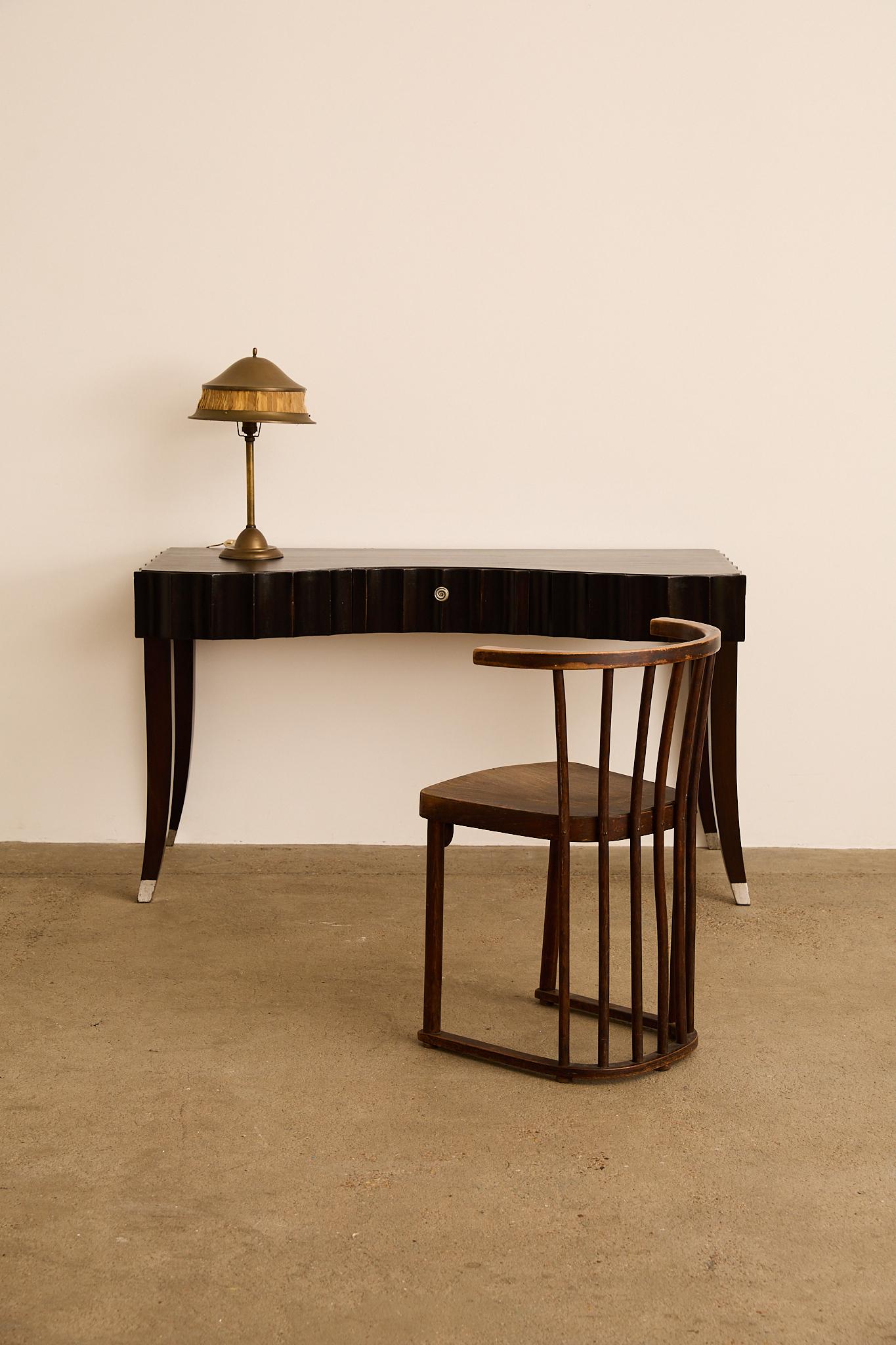 Sculptural writing desk featuring a carved wave-front apron, single central drawer with metal pull, and elegantly splayed legs finished with silver sabots. The dark lacquered finish and rhythmic front profile give the piece a strong, architectural