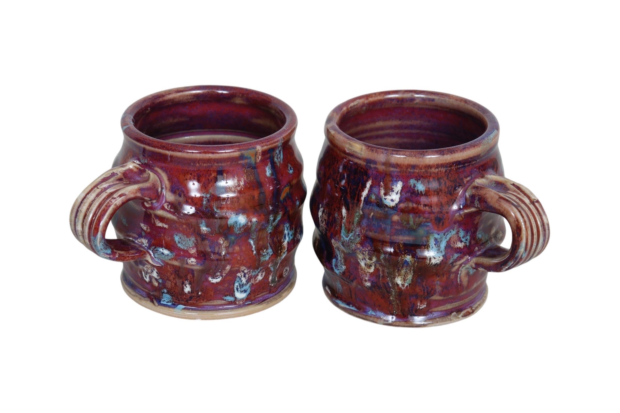 Paire de mugs en grès à glaçure goutte à goutte assortis, fabriqués à la main par l'artiste et céramiste Ron Korczynski. Les extérieurs en forme de tonneau sont nervurés avec quatre bandes pour une prise en main confortable, et décorés de bruns, de