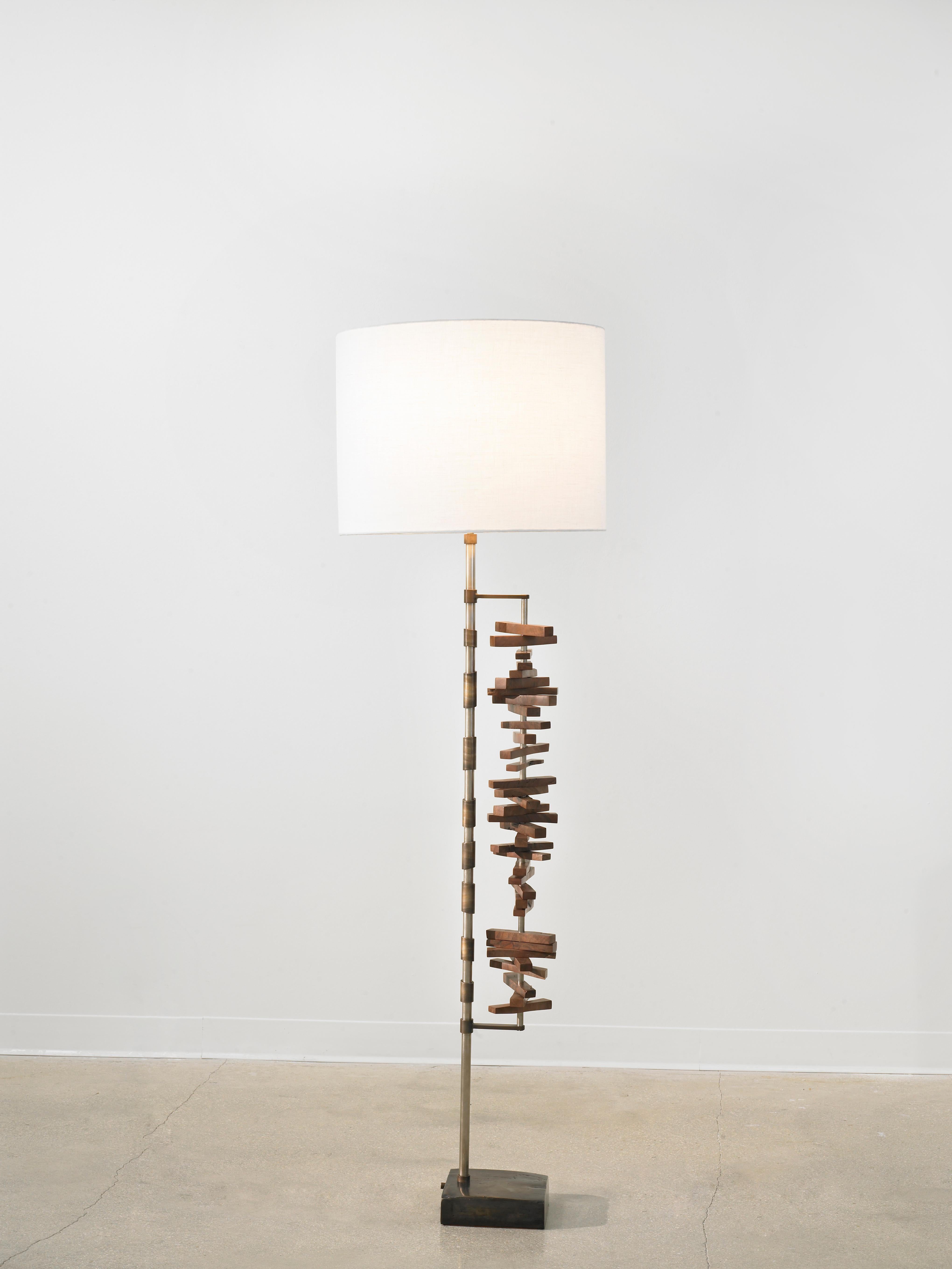 The 'Vela' floor lamp was inspired by tribal wood carvings that embody the balance between repetition and uniqueness. Each lamp is one of a kind due to the individual qualities of the walnut pieces used. No two are alike.
