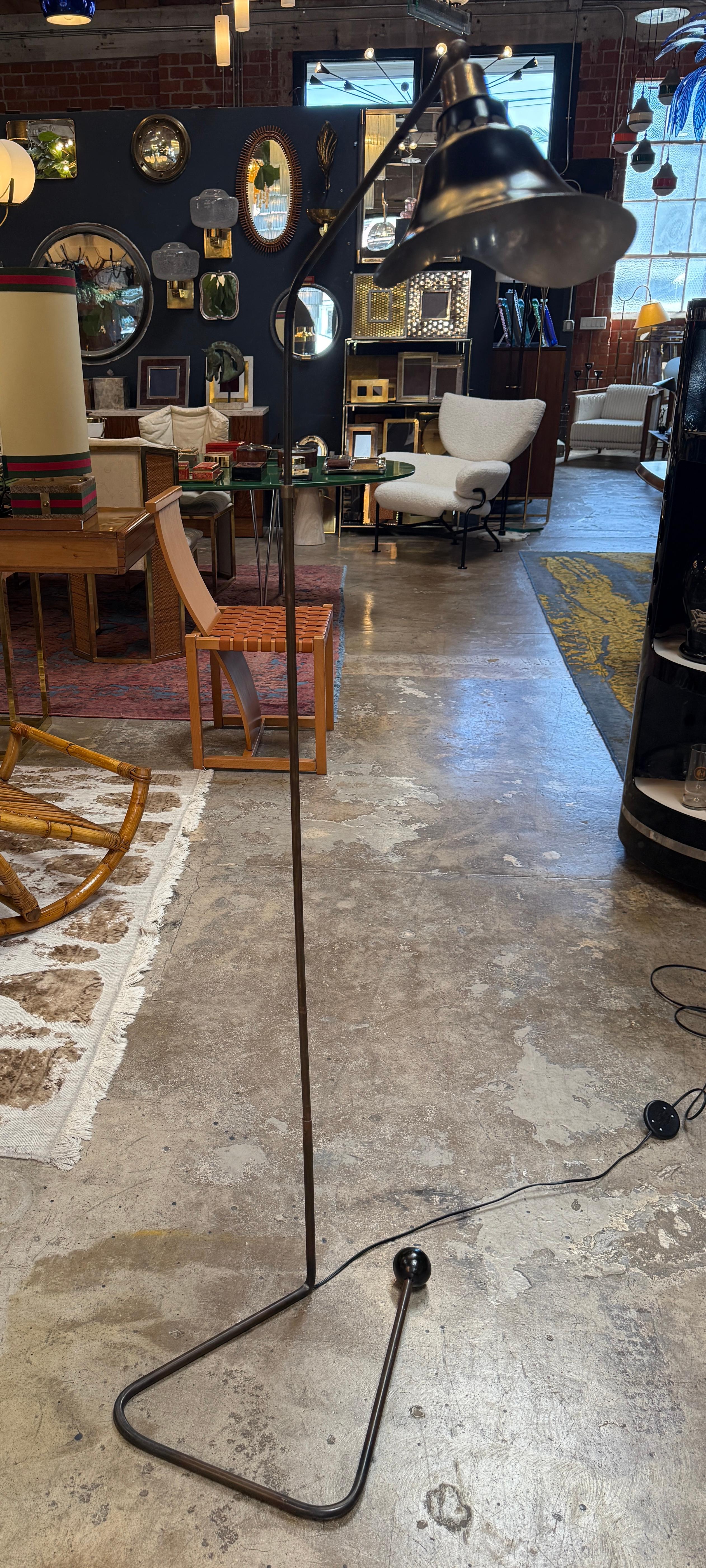 An expressive Italian floor lamp from the 1950s, featuring a slender, angular stem that extends into a sculptural bent base balanced on a ball foot. The lamp is crowned with an organically shaped metal shade that tilts gently, casting focused