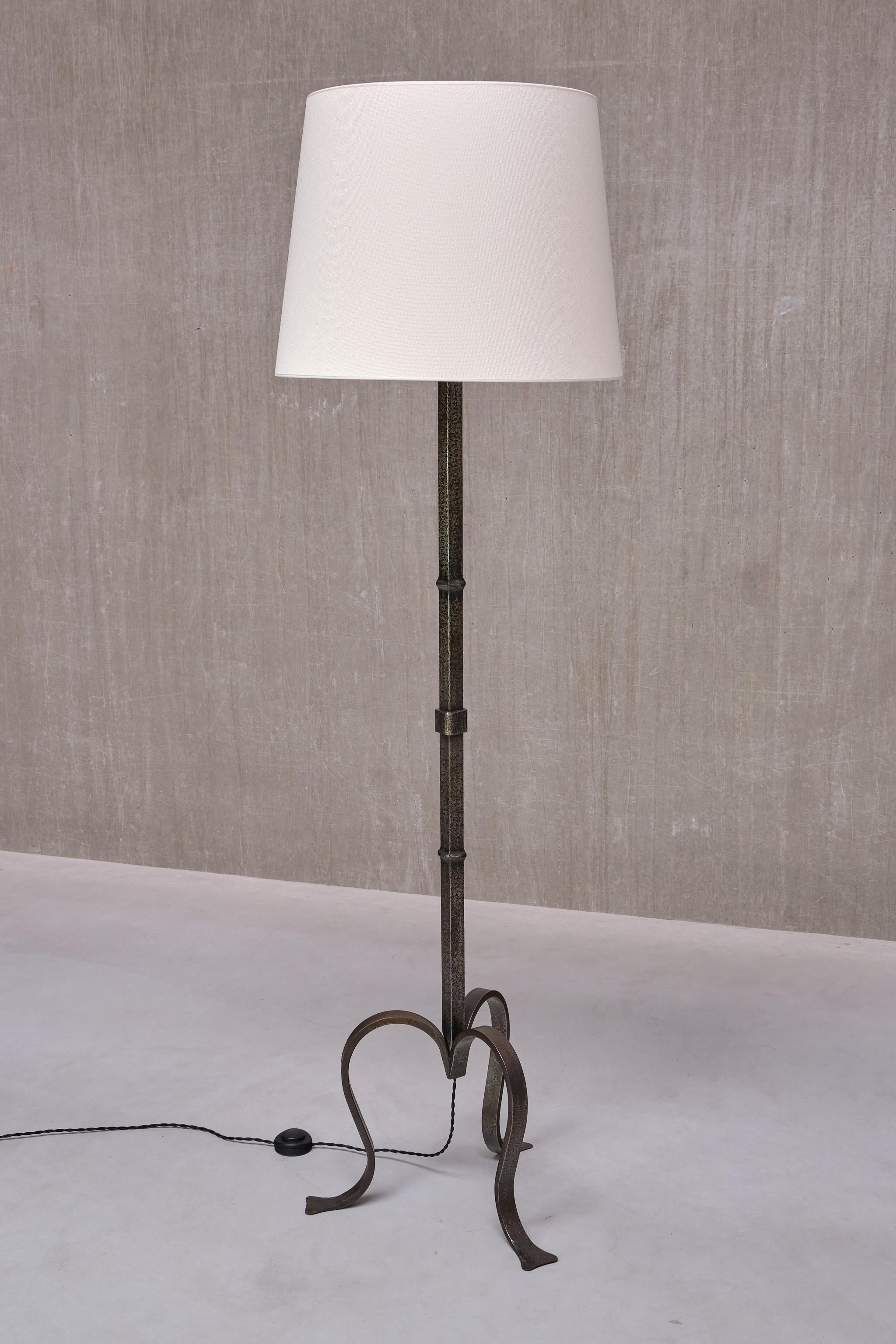 This rare three-legged floor lamp was manufactured in France in the early 1950s. 

The striking base is marked by the three sculptural, curved legs ending in striking flat feet. The entire lamp was produced by hand in a natural wrought iron which