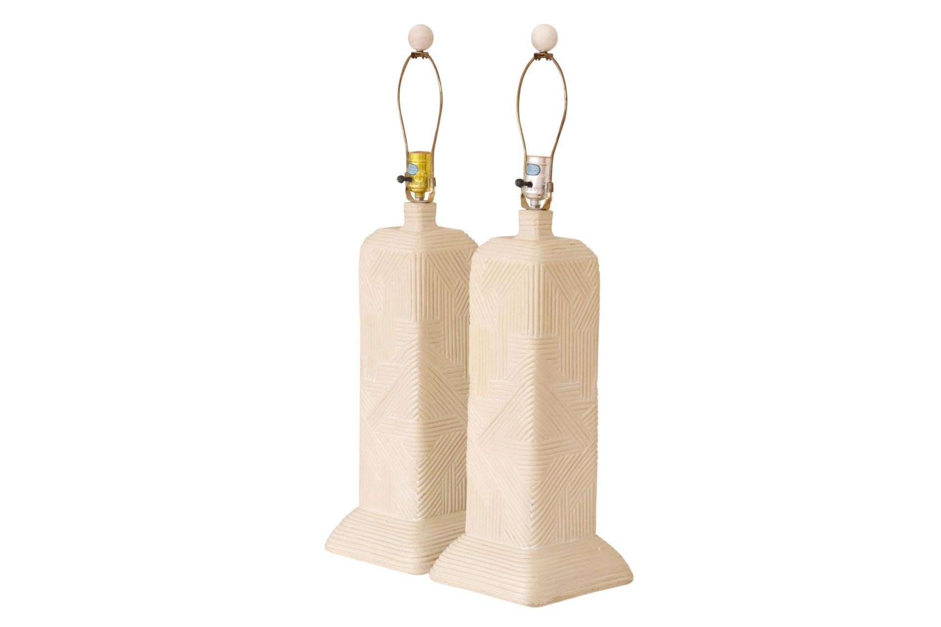 A pair of sculptural table lamps with a southwestern style. Made of plaster and cast with geometric lines that give the look of pencil-wood bamboo. Harps are topped with ball finials. Each lamp measures 22.5