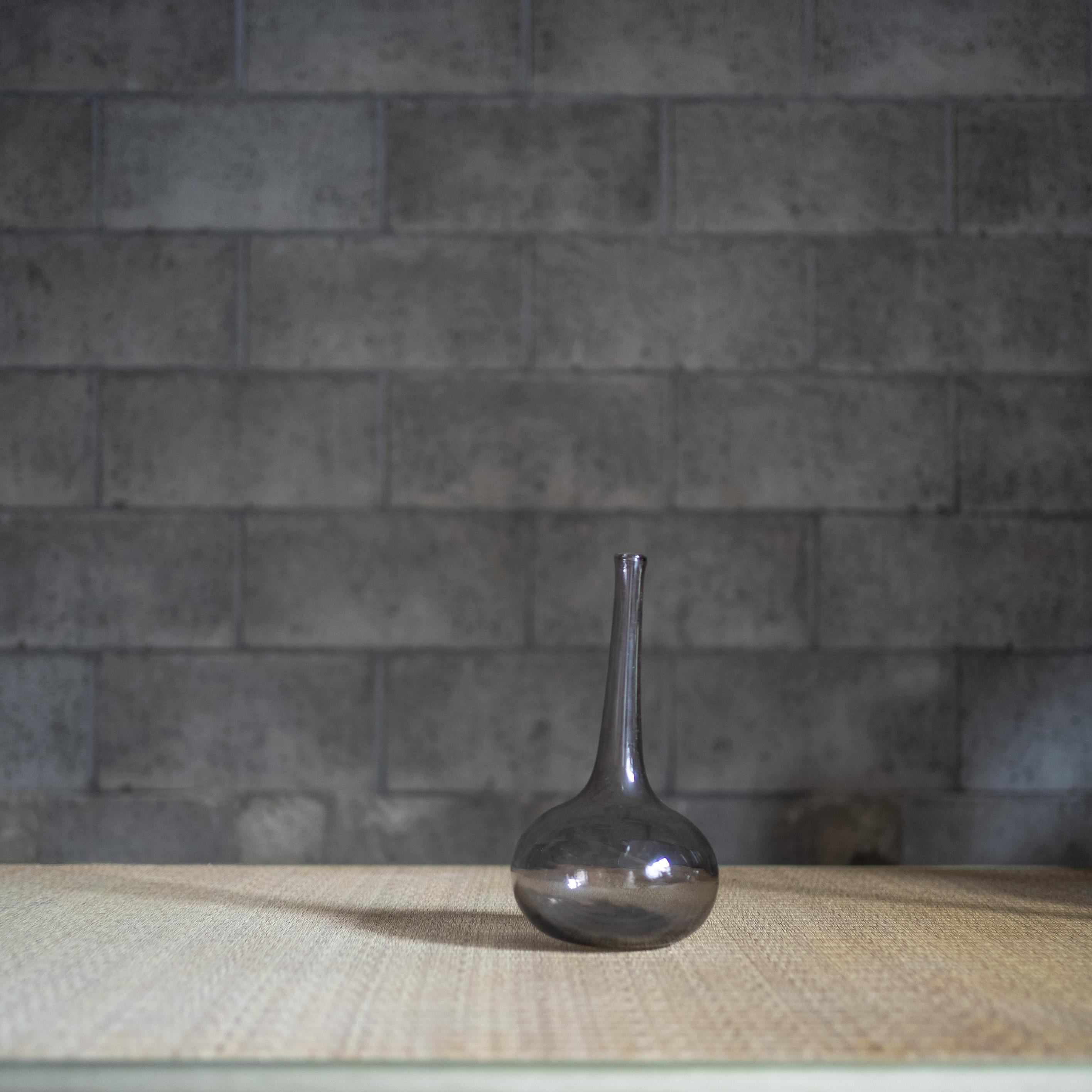 Eine Vase aus mundgeblasenem Glas des französischen Künstlers Claude Morin. Der langgestreckte Hals erhebt sich elegant von einem abgerundeten Sockel und unterstreicht das Gefühl von Balance und Leichtigkeit. Der subtile rauchige Ton des Glases