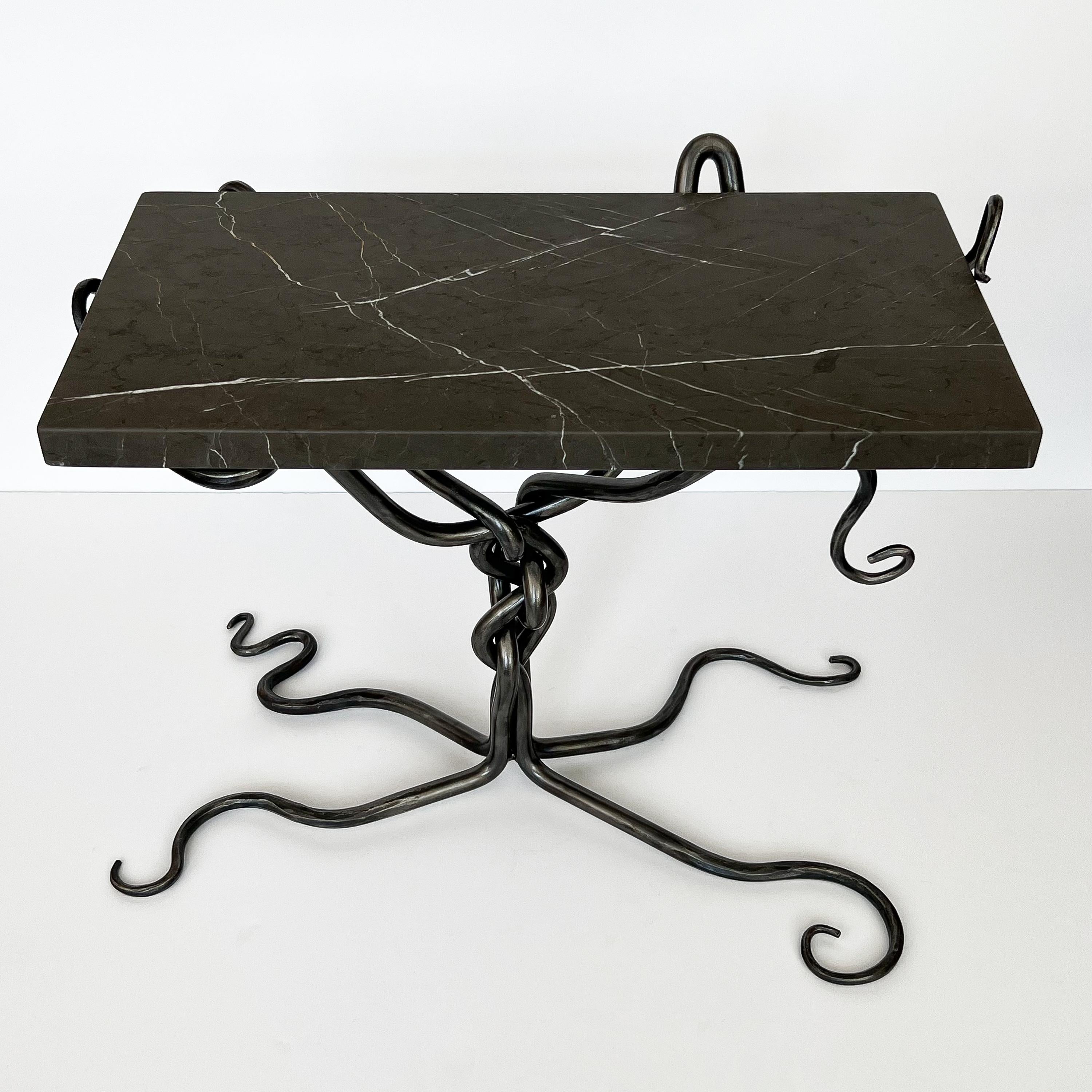 A spectacular hand-forged steel end or side table with marble top, circa late 20th century. Unmarked and unknown artist. Four separate forged steel bars are interwoven creating a central twisted knot, four splayed snaking legs and supports for the
